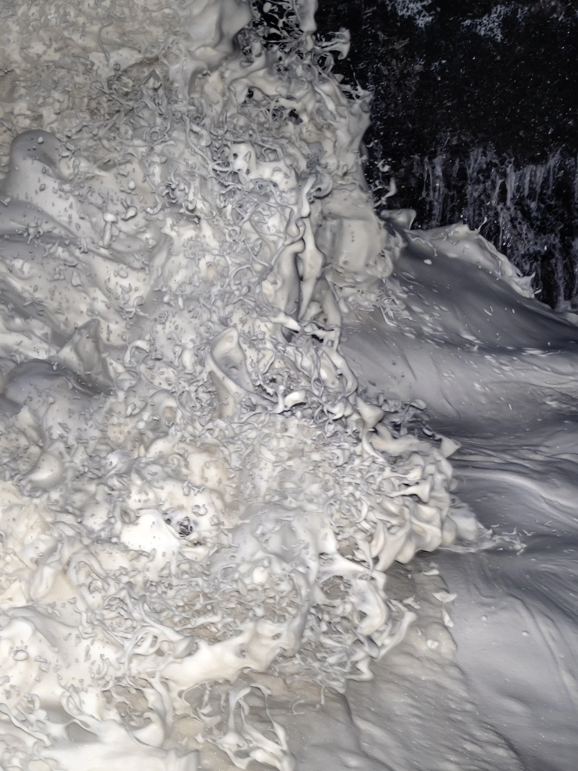 A close-up of white foam and dark water creating a foamy, swirling pattern.