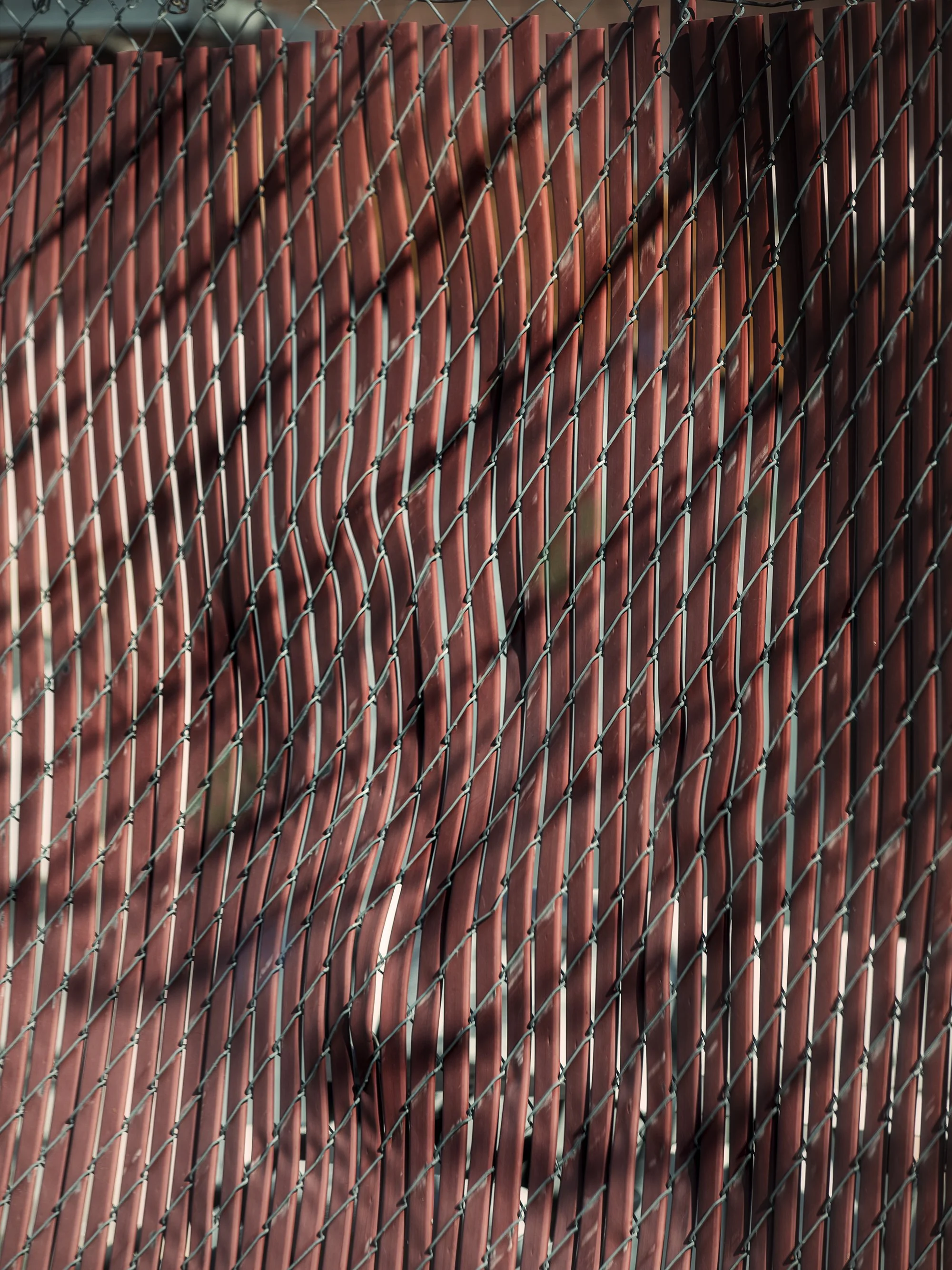 Close-up of a chain-link fence with red wooden slats behind it, creating a textured background.