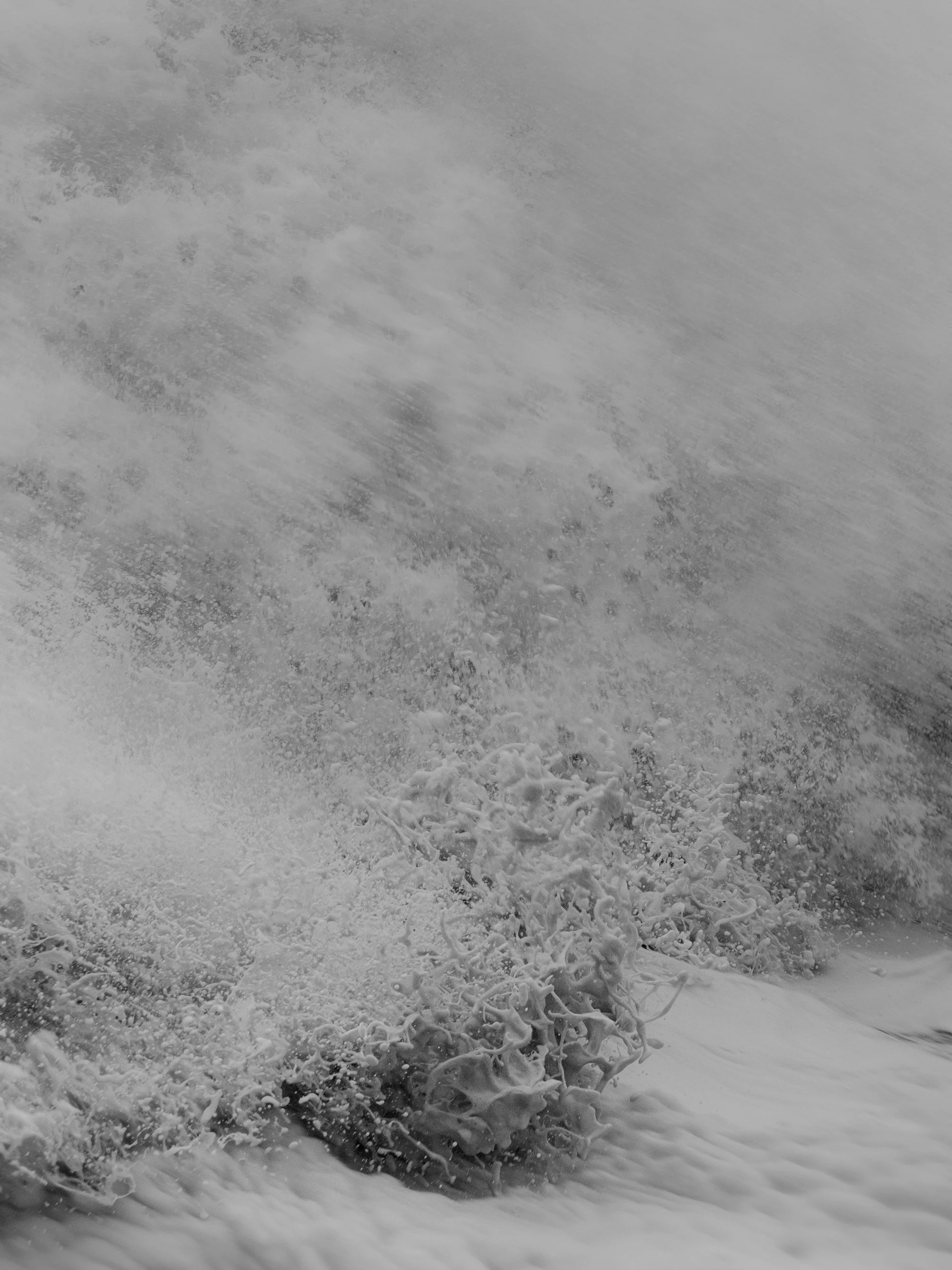 A close-up of a turbulent splash of snow or ice, with snow-covered ground and some twigs or branches at the bottom.