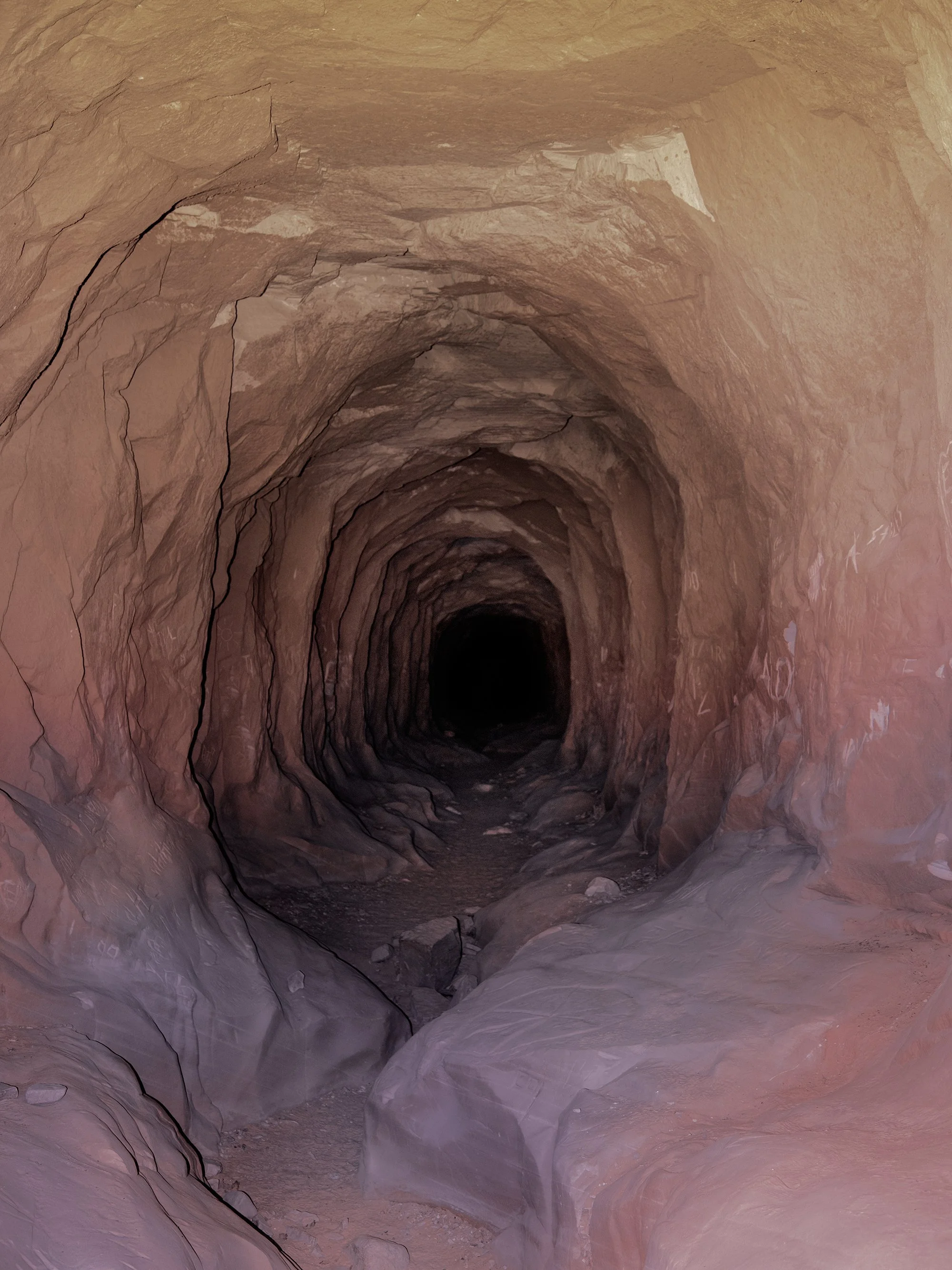 A photo of the inside of a pink and reddish cave with rocky, textured walls and a dark passageway stretching into the distance.