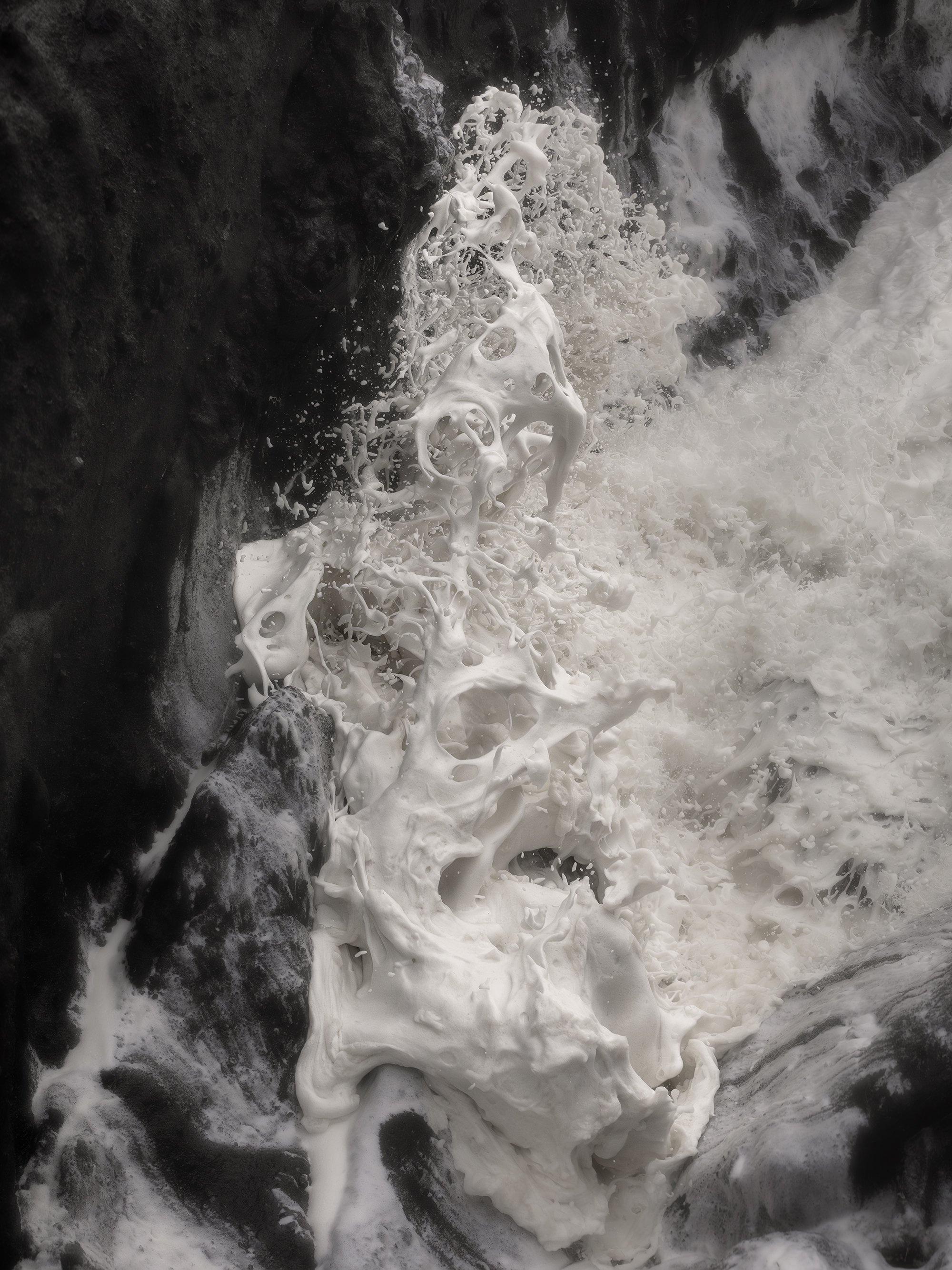 Ocean waves crashing against black rocks, creating white foam and spray.