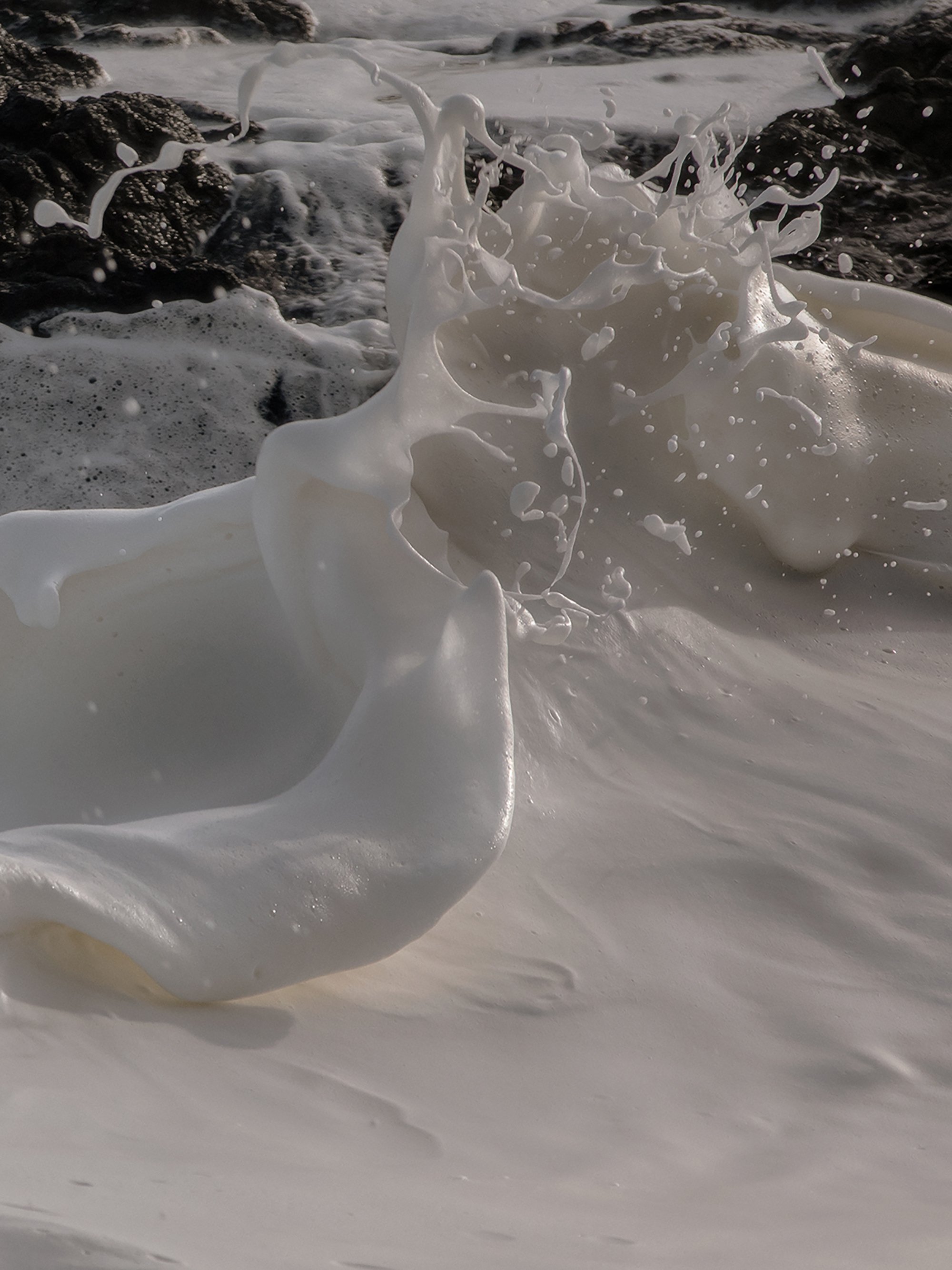 Close-up of sea foam crashing onto rocks on the beach.