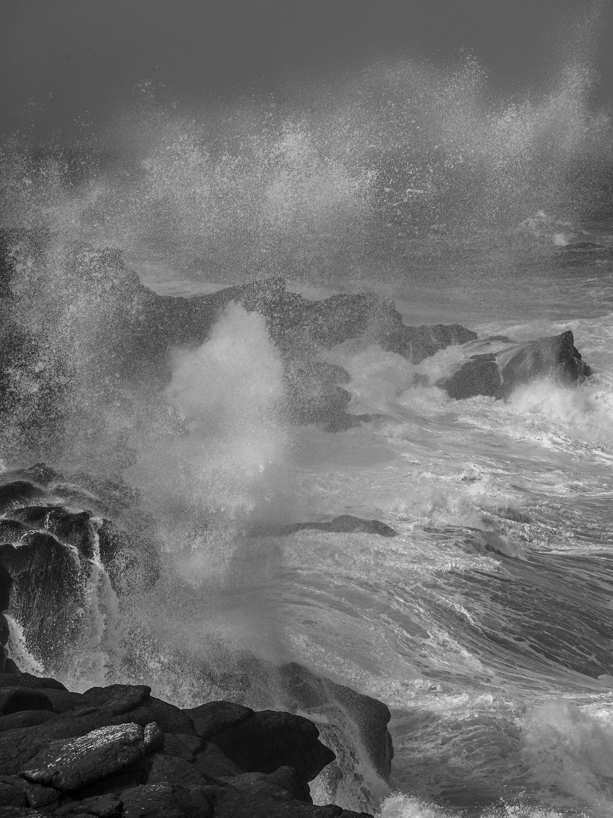 Black and white photograph of ocean waves crashing against rocks during a storm.