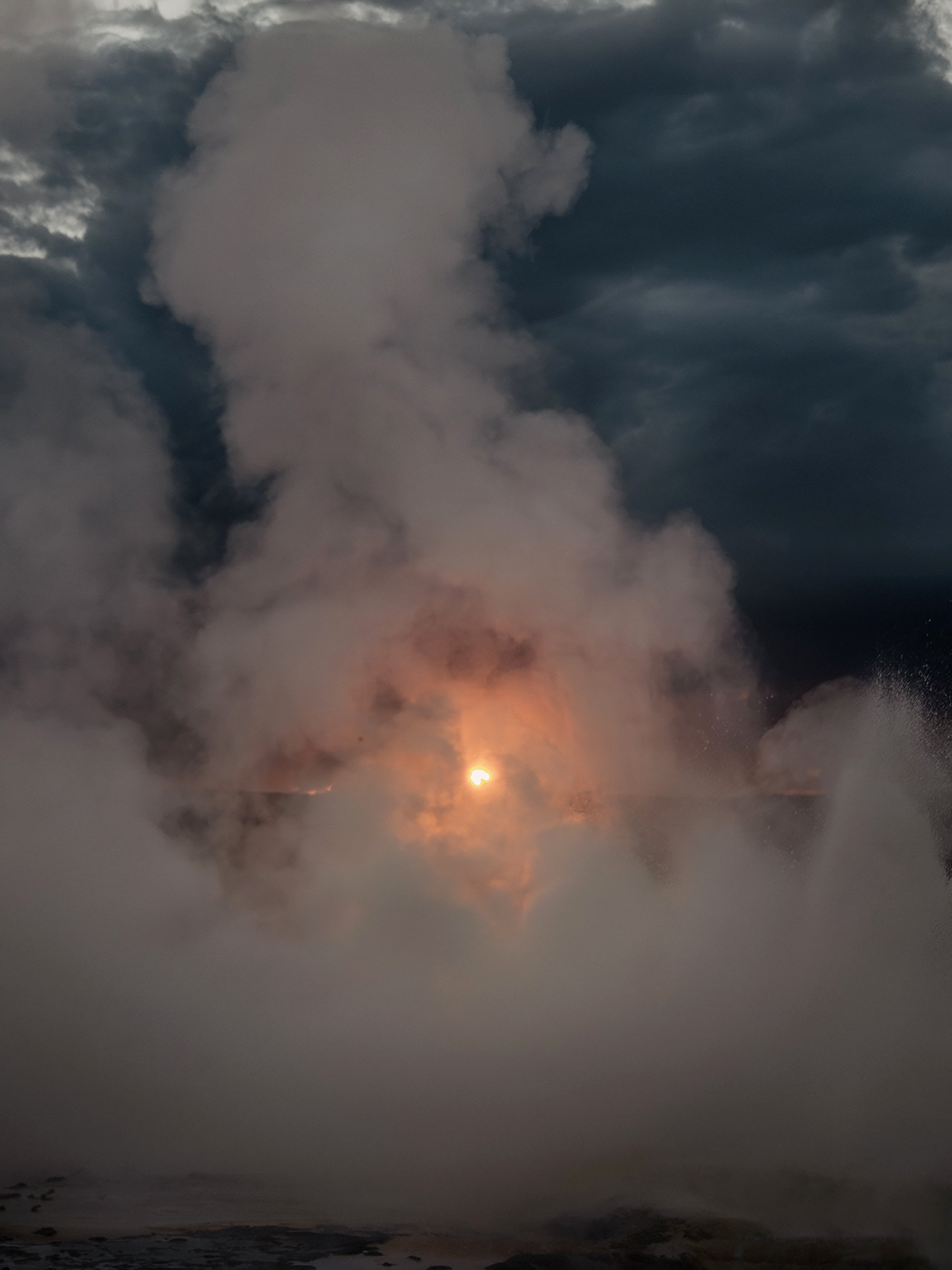 Sunset over the ocean with dark clouds, and the sun partially hidden by the clouds near the horizon.
