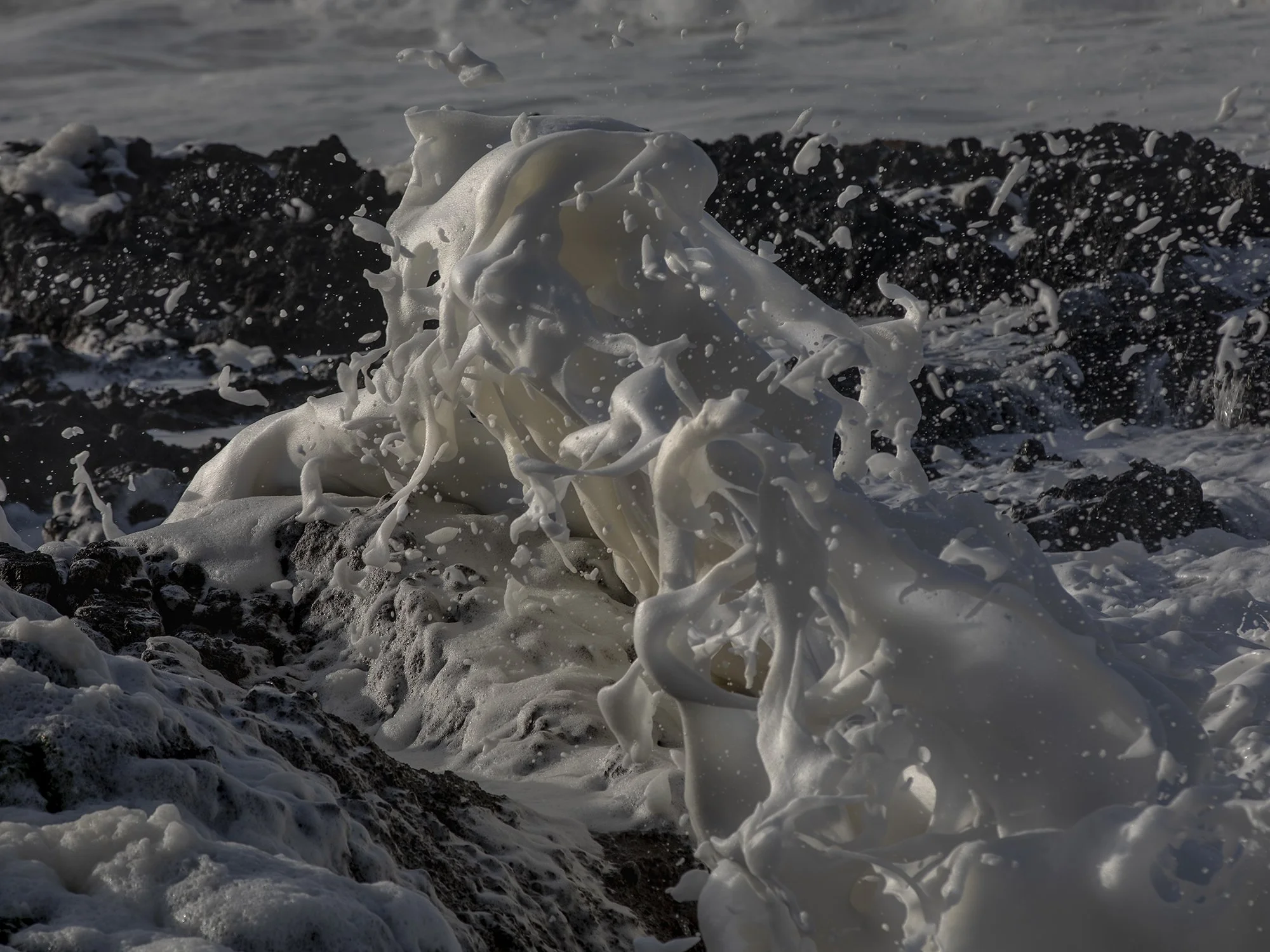 Foamy ocean waves crashing against dark rocks with white sea foam splashing into the air.