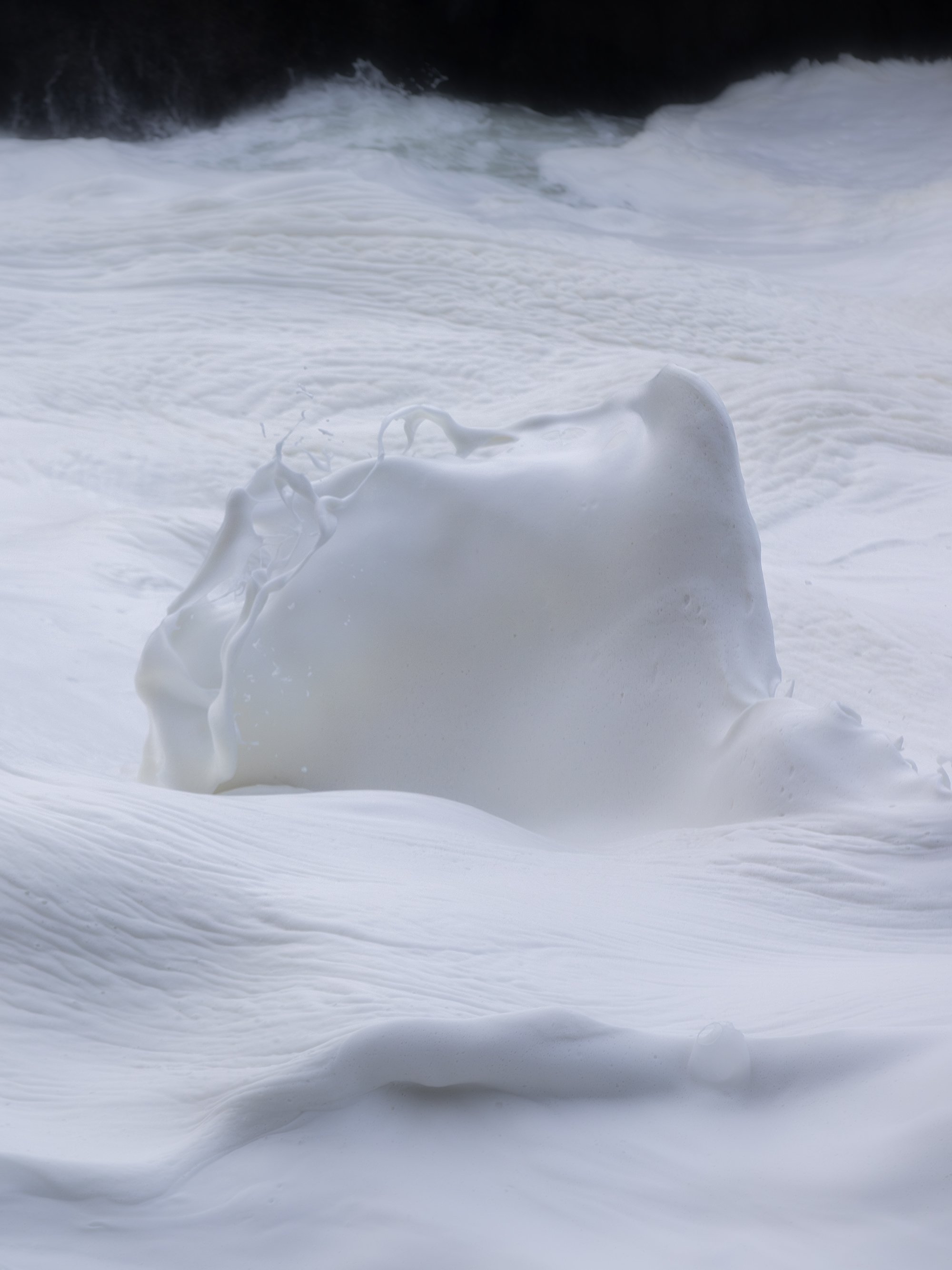 A large wave crashing onto the shore, sending white foam into the air during a stormy sea.