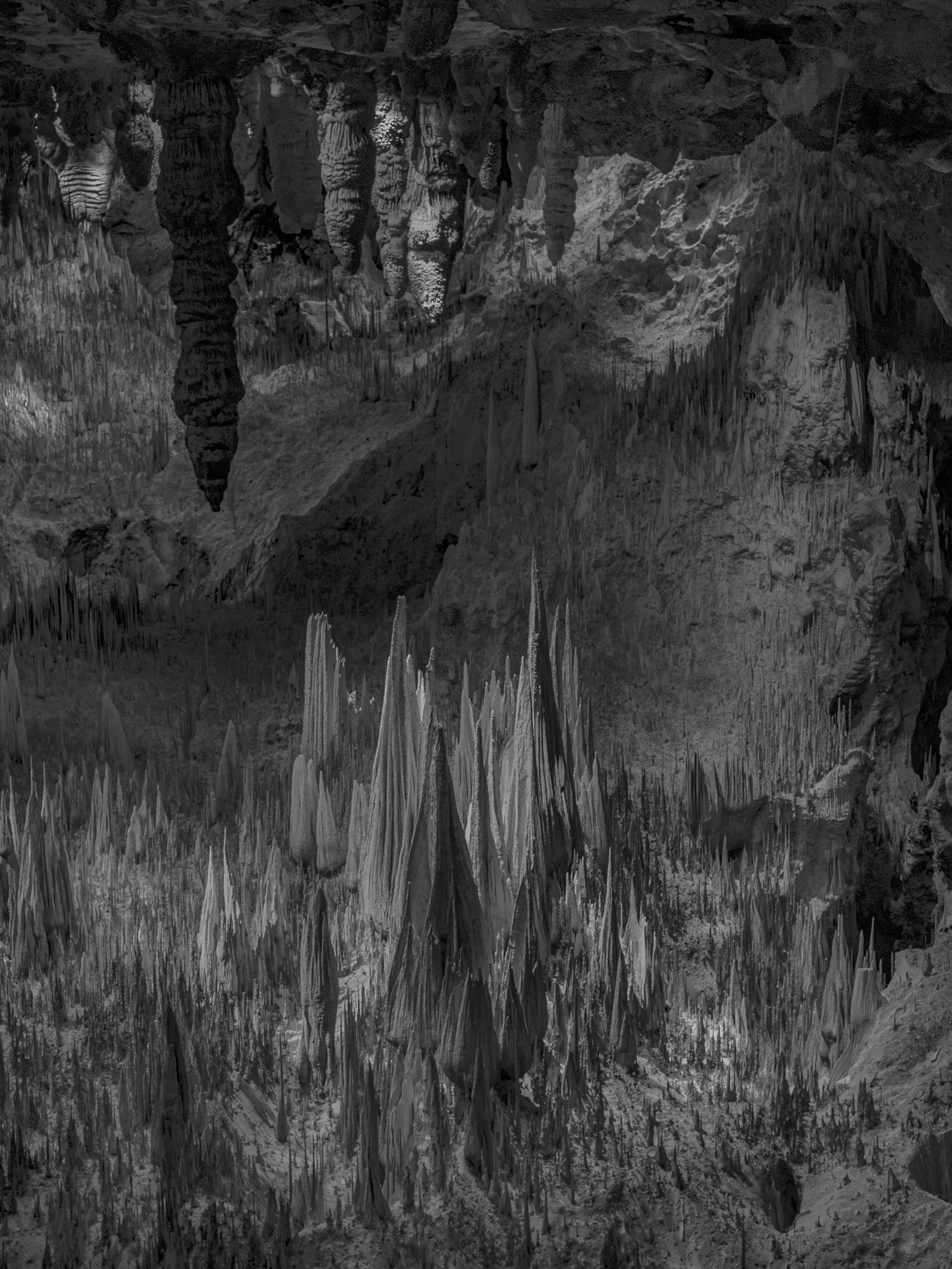 A black-and-white photo of a cave with stalactites hanging from the ceiling and stalagmites rising from the ground.