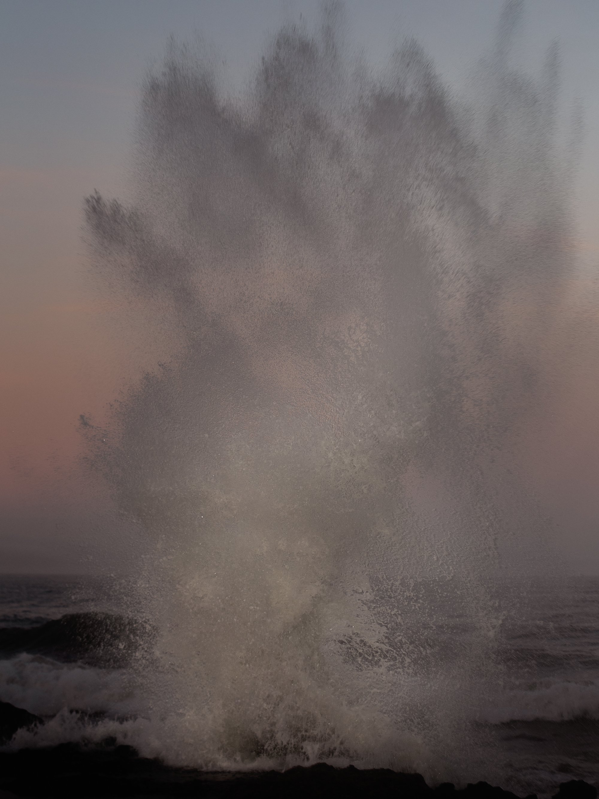 Wave crashing against the shoreline during sunset with a pink and purple sky.