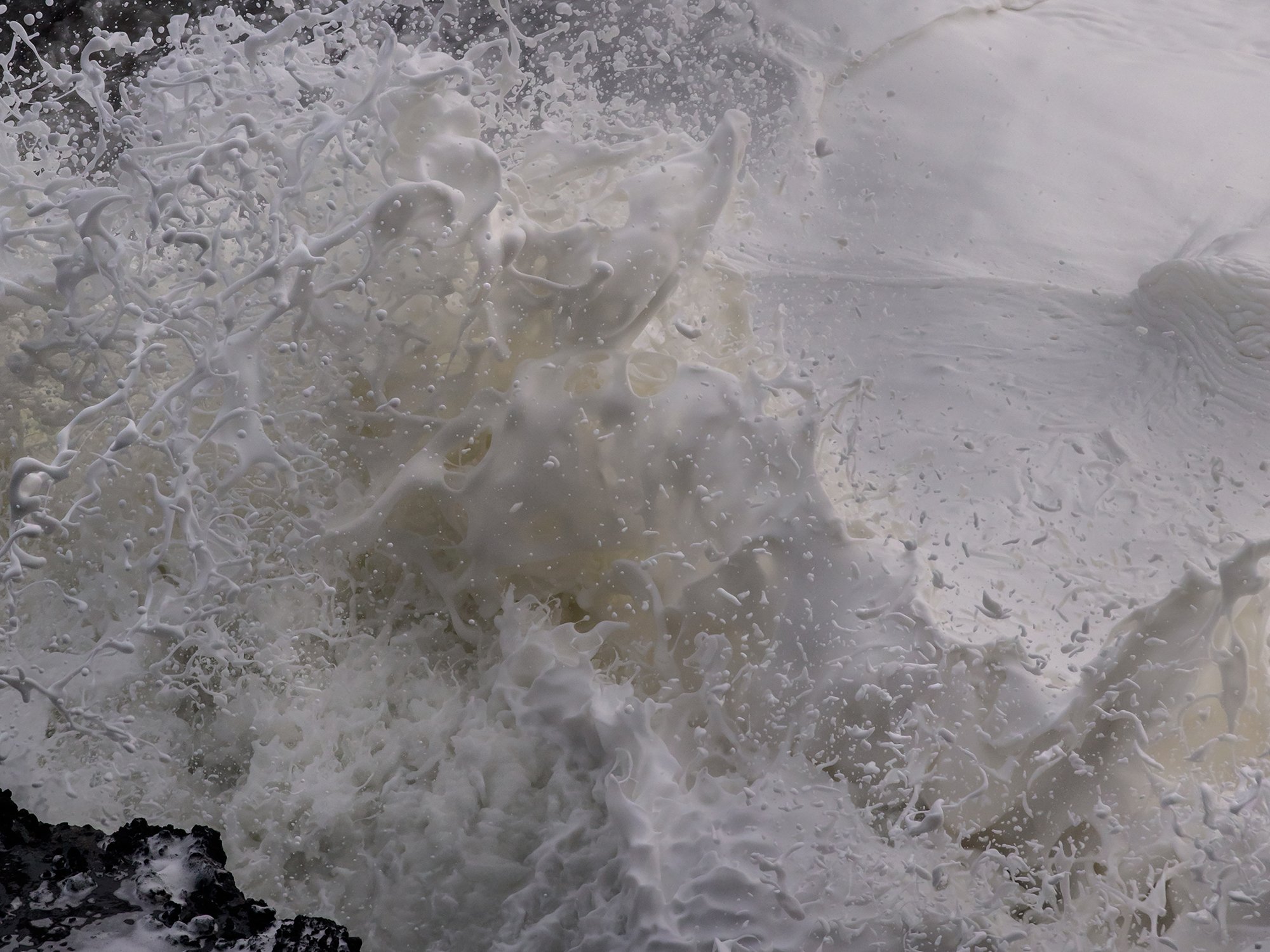 Ocean waves crashing against rocks, with white foamy splashes and spray in the air.