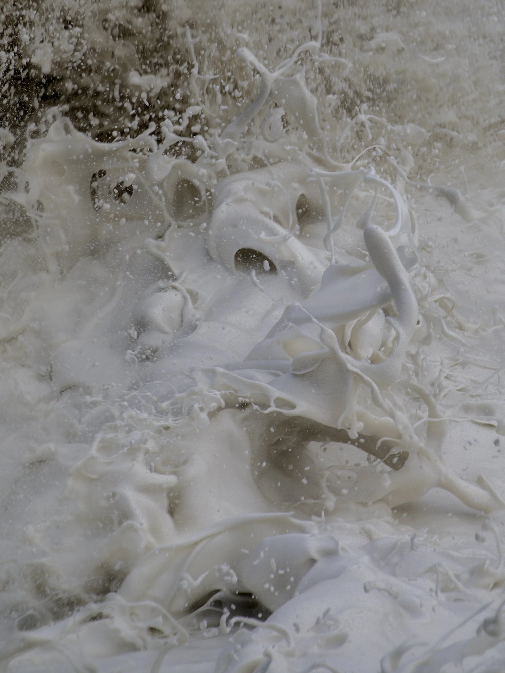 Close-up of white liquid splashing and swirling, creating a dynamic pattern of foam and droplets.