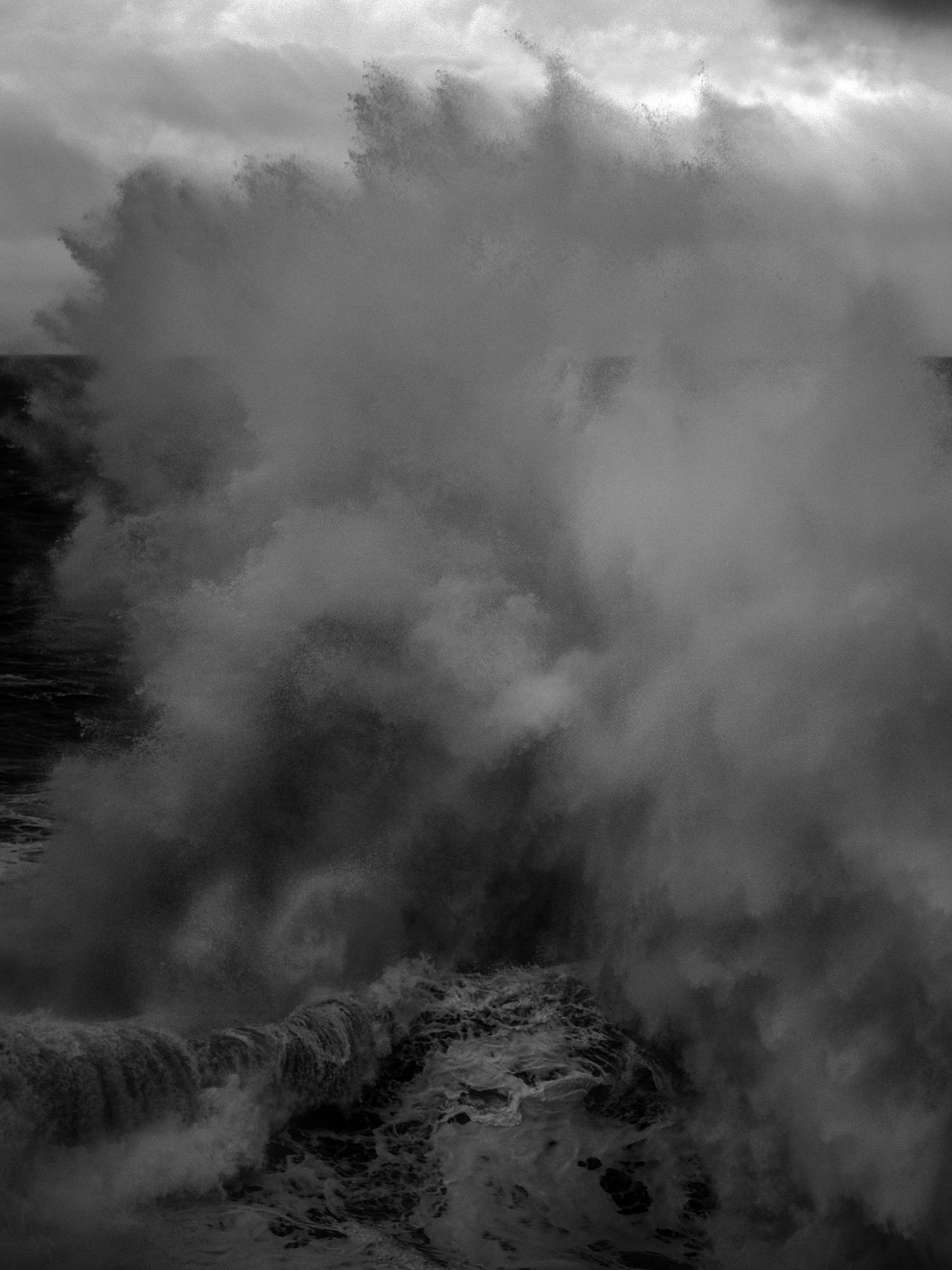 A large ocean wave crashing onto rocks during a stormy day with dark cloudy sky.