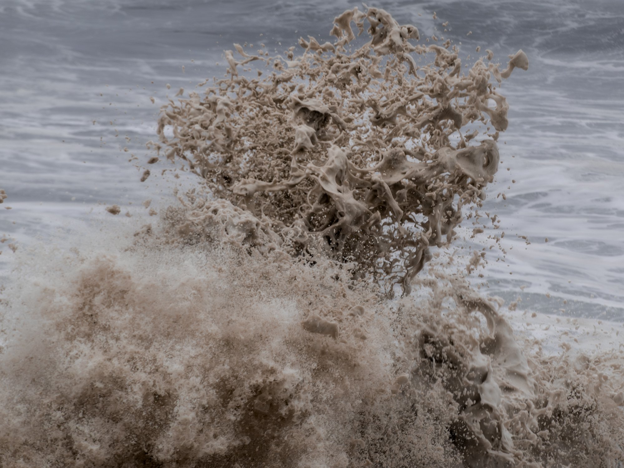 Wave crashing onto the shore with brownish foam and sea spray.