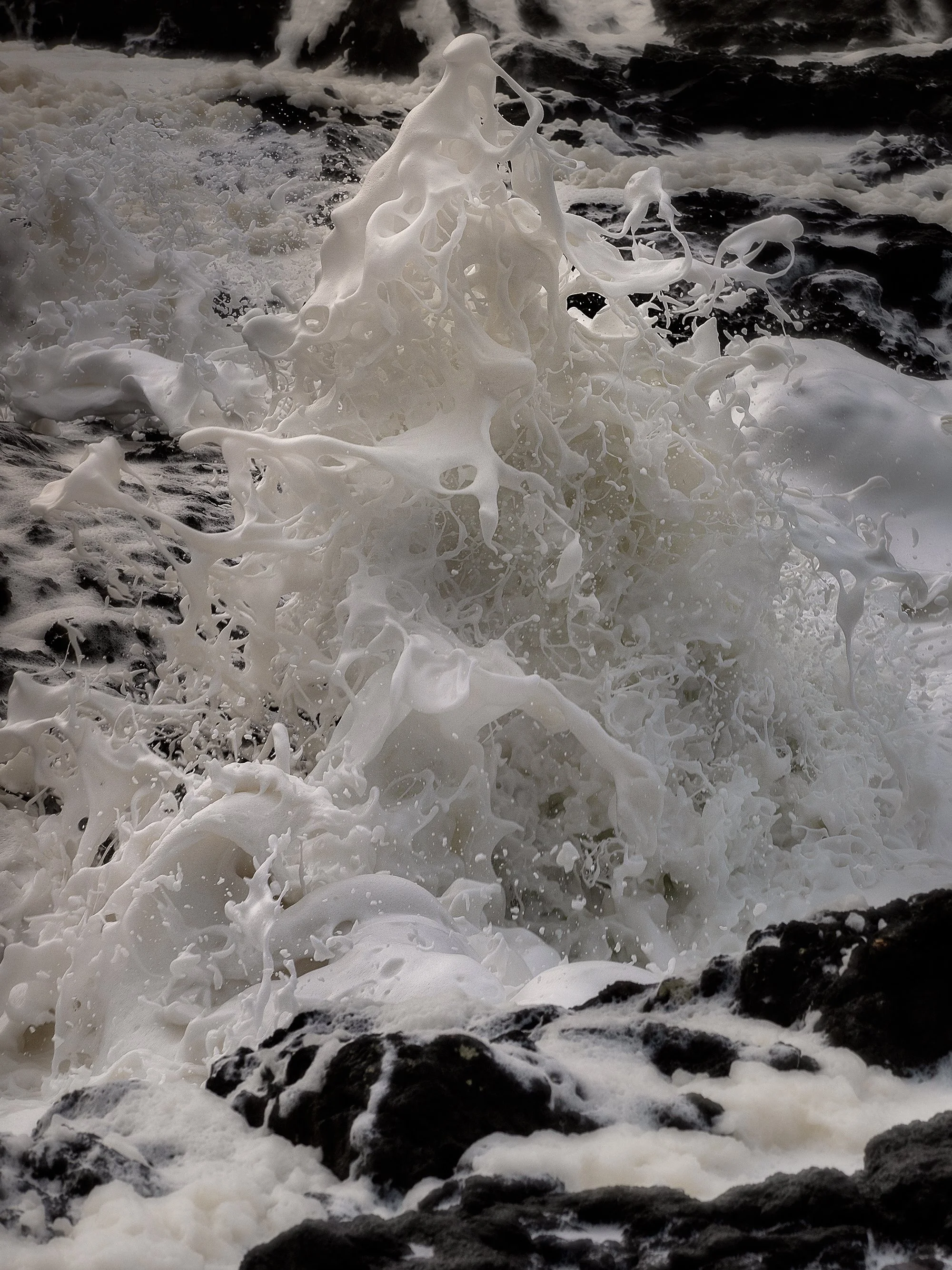 Waves crashing against rocks with foam and spray at the shoreline.