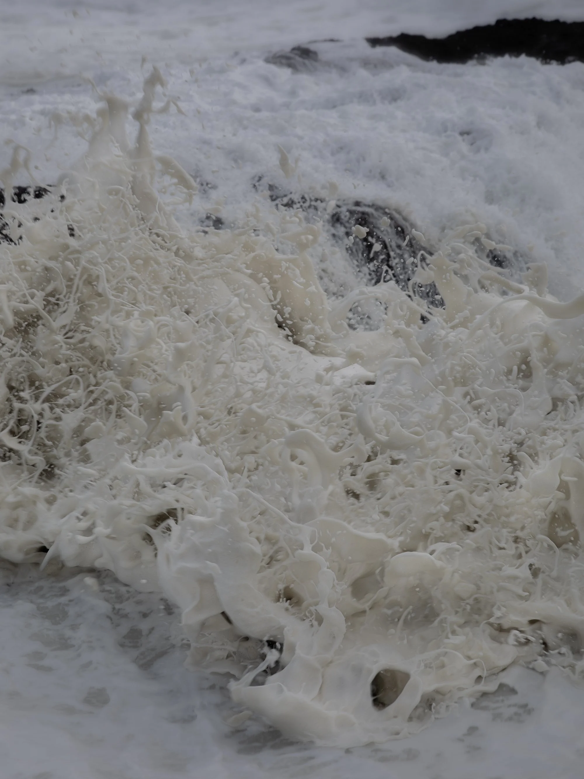 Large waves crashing against rocks, creating foam and spray at the ocean shoreline.