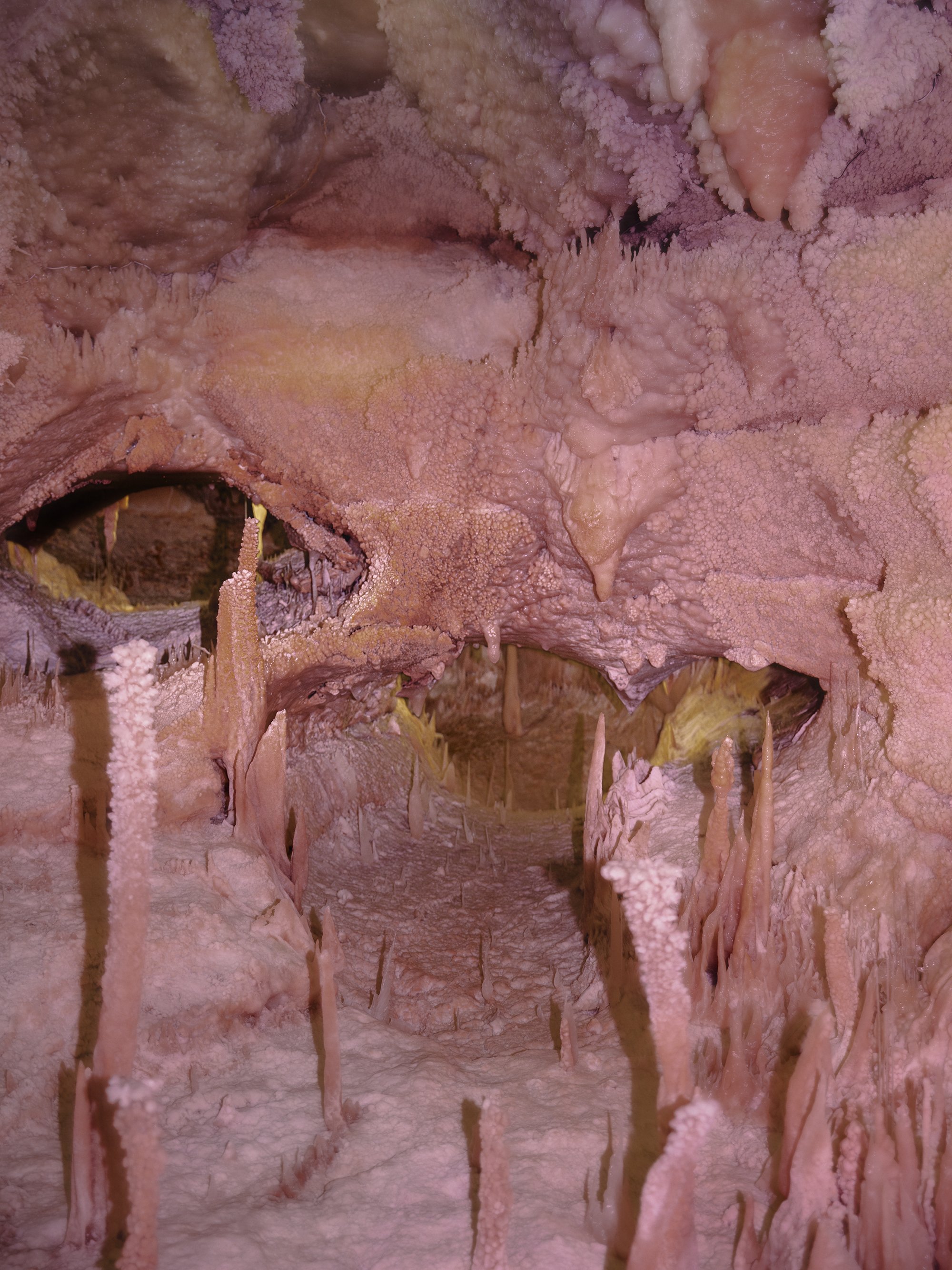Close-up of cave formations with stalactites and stalagmites in shades of pink and orange.