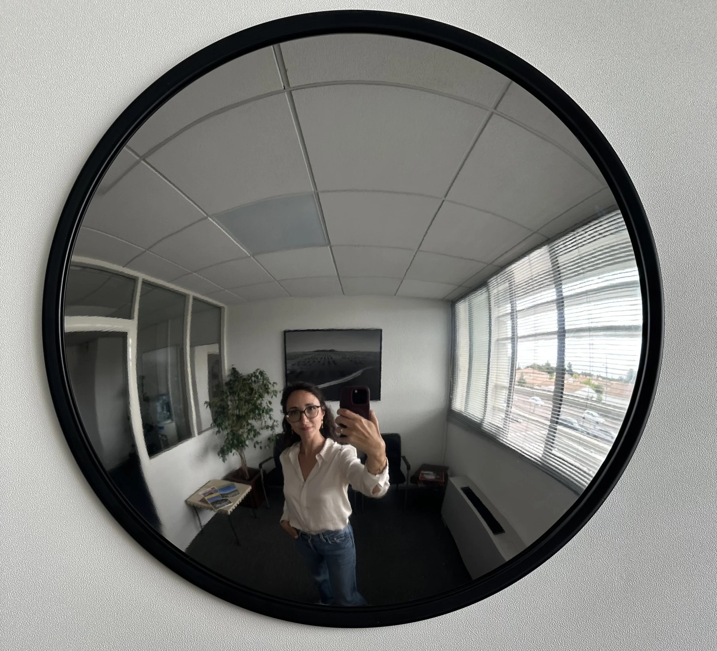 Une femme prenant un selfie dans un miroir rond avec un plafond et une fenêtre en arrière-plan.