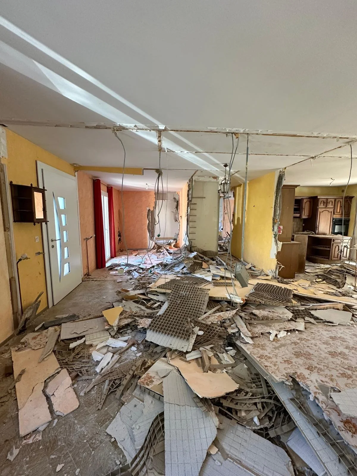 Une pièce en désordre après une démolition avec des décombres, des câbles suspendus, et des murs endommagés.