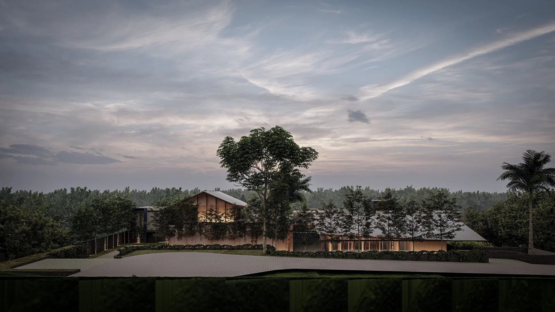 A building with a metal roof surrounded by trees, with a large tree in the foreground and a cloudy sky overhead during sunset.