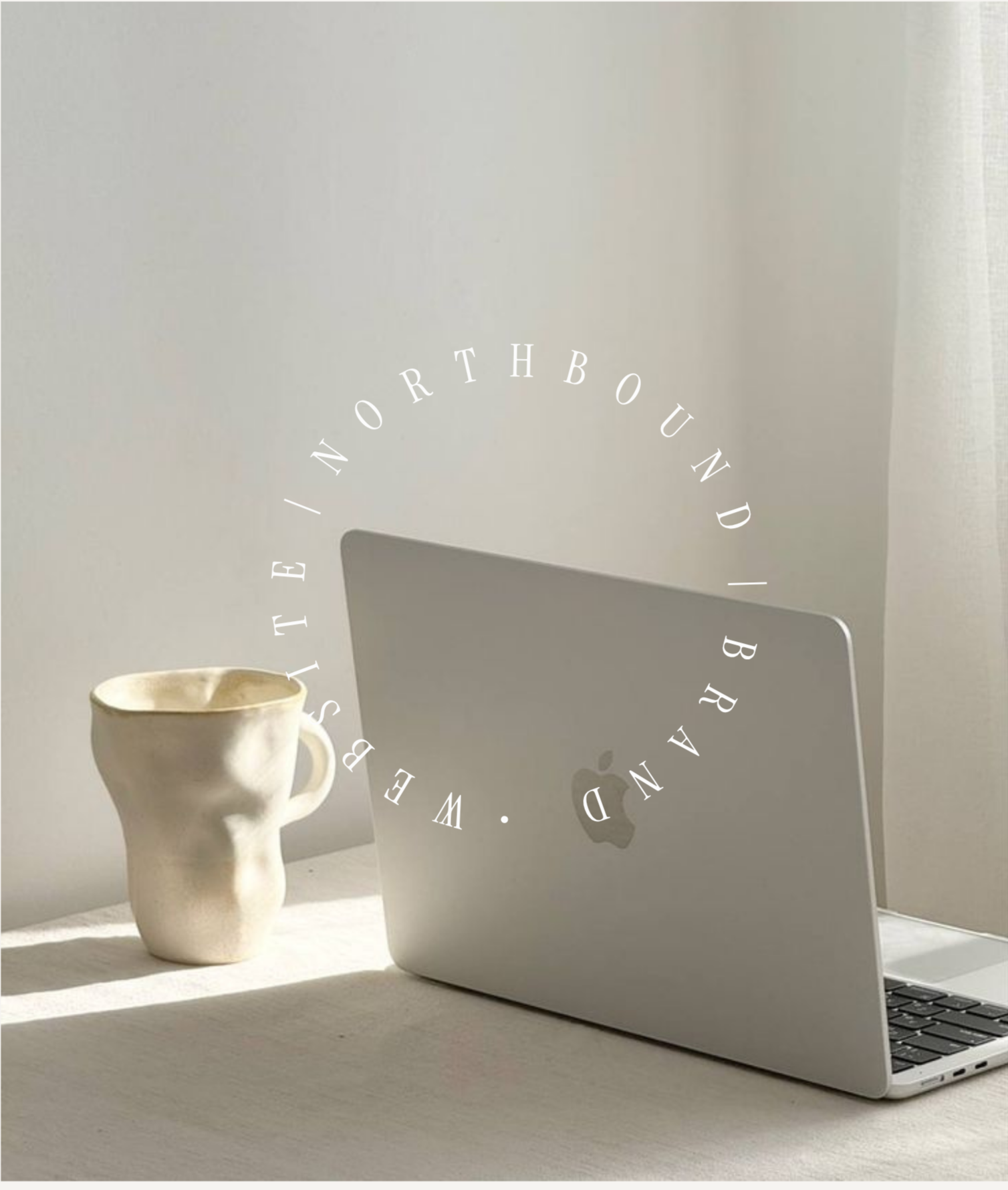 A beige ceramic mug shaped like a human face with a raised nose and closed eyes, placed next to a silver laptop and a white wall with natural light.