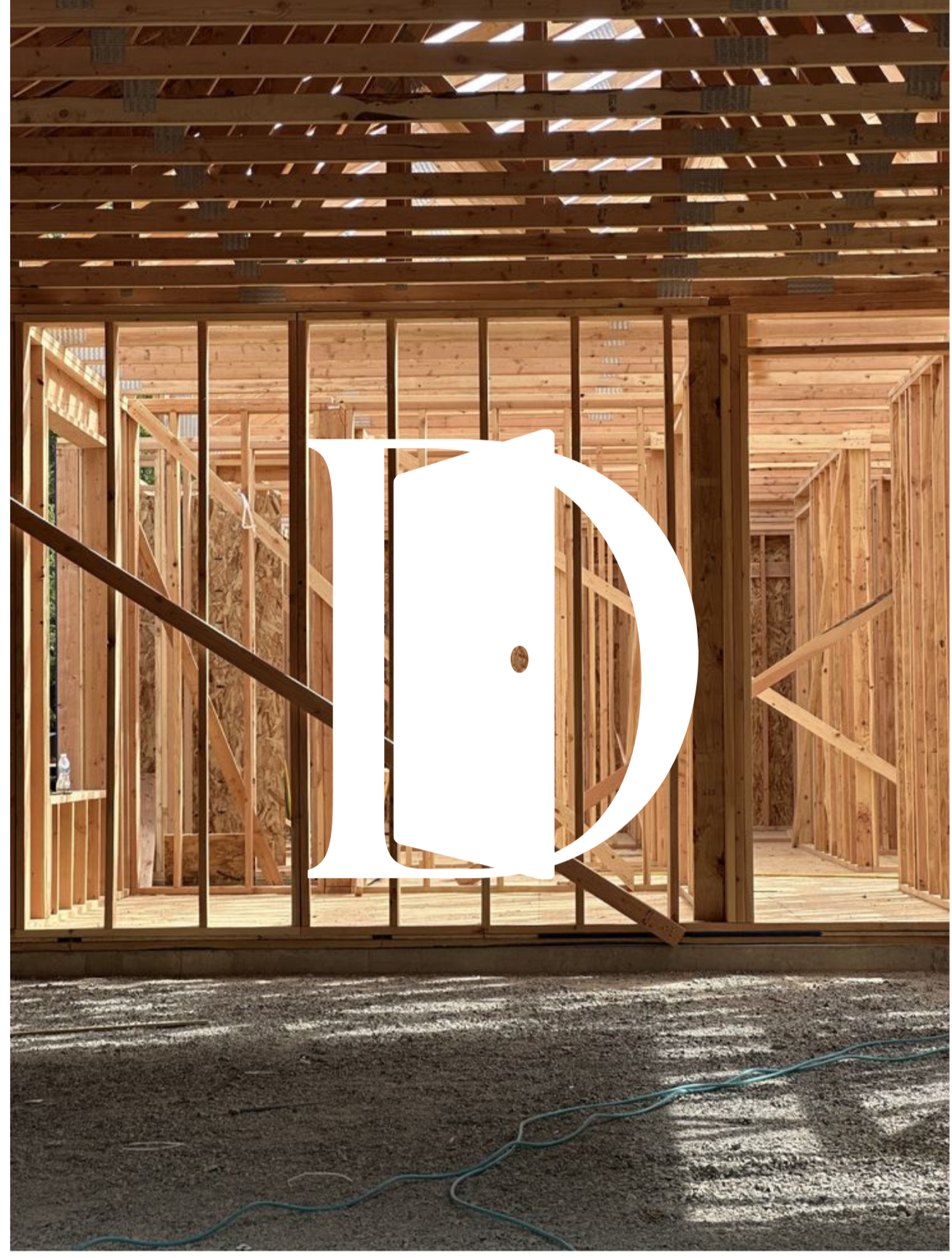 Interior framing of a wooden house under construction, showing vertical and horizontal wooden studs and roof beams, with sunlight filtering through gaps.