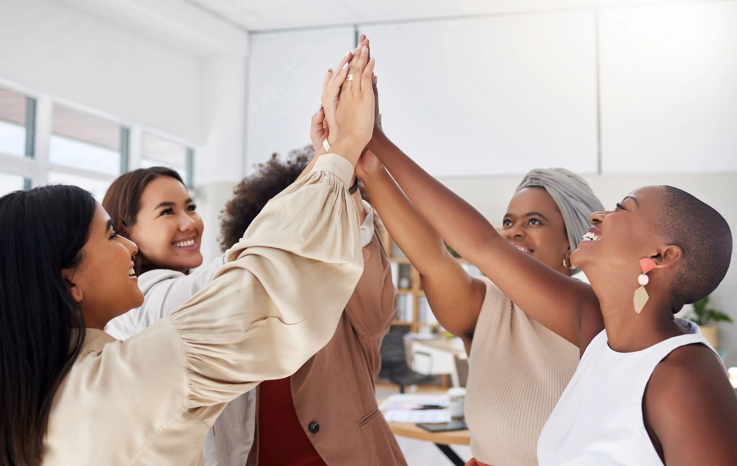 Group of diverse women in an office high-fiving each other cheerfully.