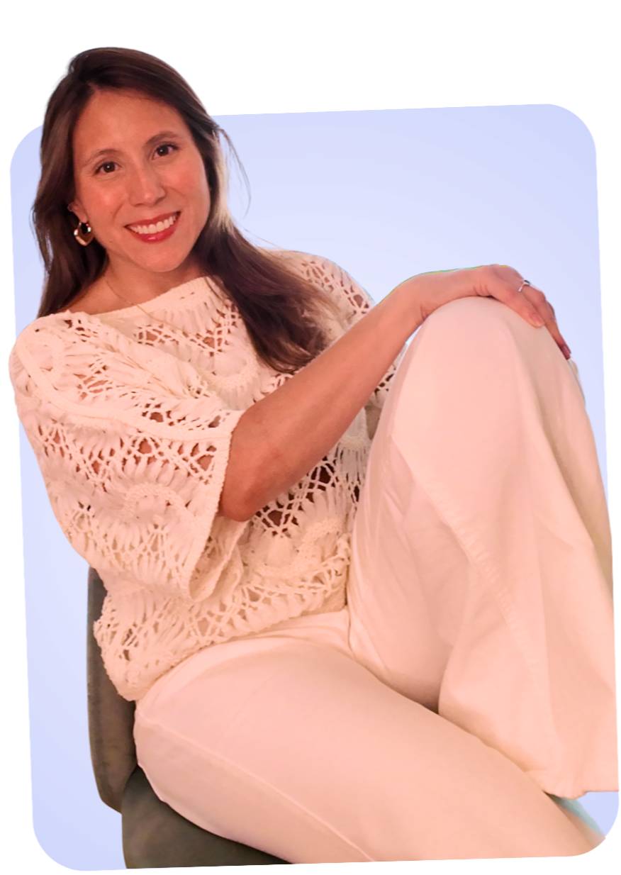 Mujer sonriendo con ropa de encaje blanca, sentada en una silla contra un fondo azul claro.