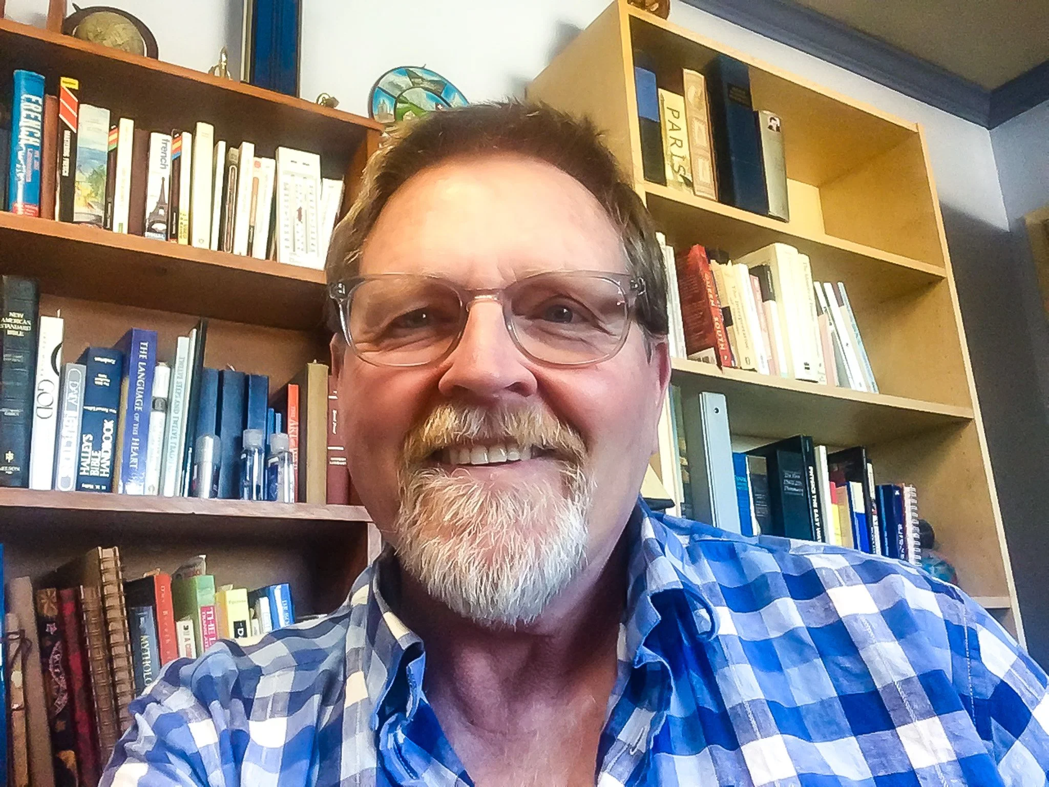 California therapist Ron Deming is seen here with glasses and a beard, smiling in front of bookshelves filled with books.
