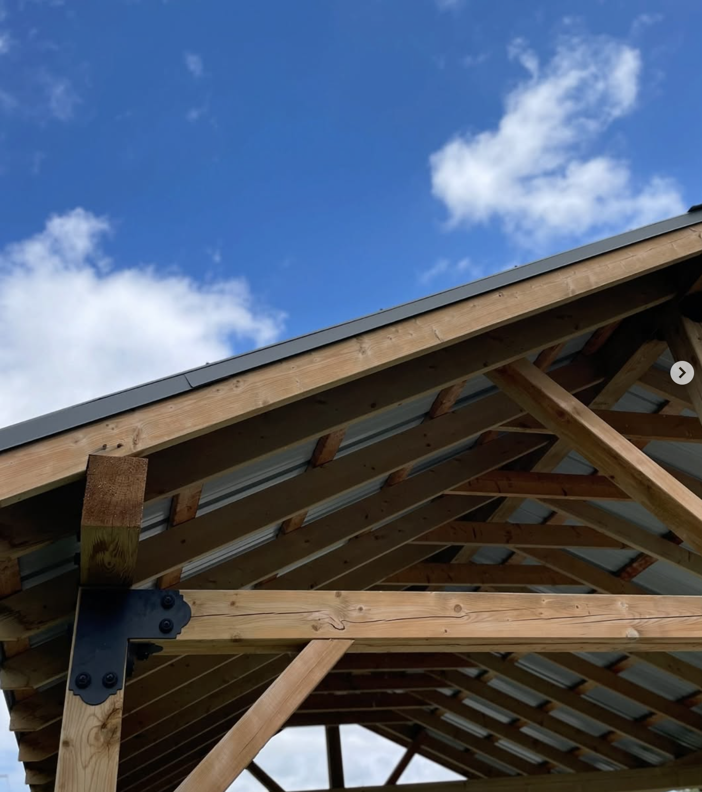 Construction of a wooden roof frame with visible trusses, beams, and metal roofing sheets under a partly cloudy blue sky.