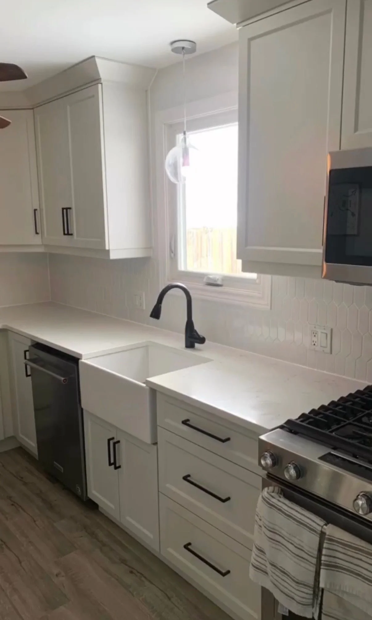 Modern kitchen with white cabinets, black hardware, a black faucet, and stainless steel appliances, including a microwave and stove, near a window with a view outside.