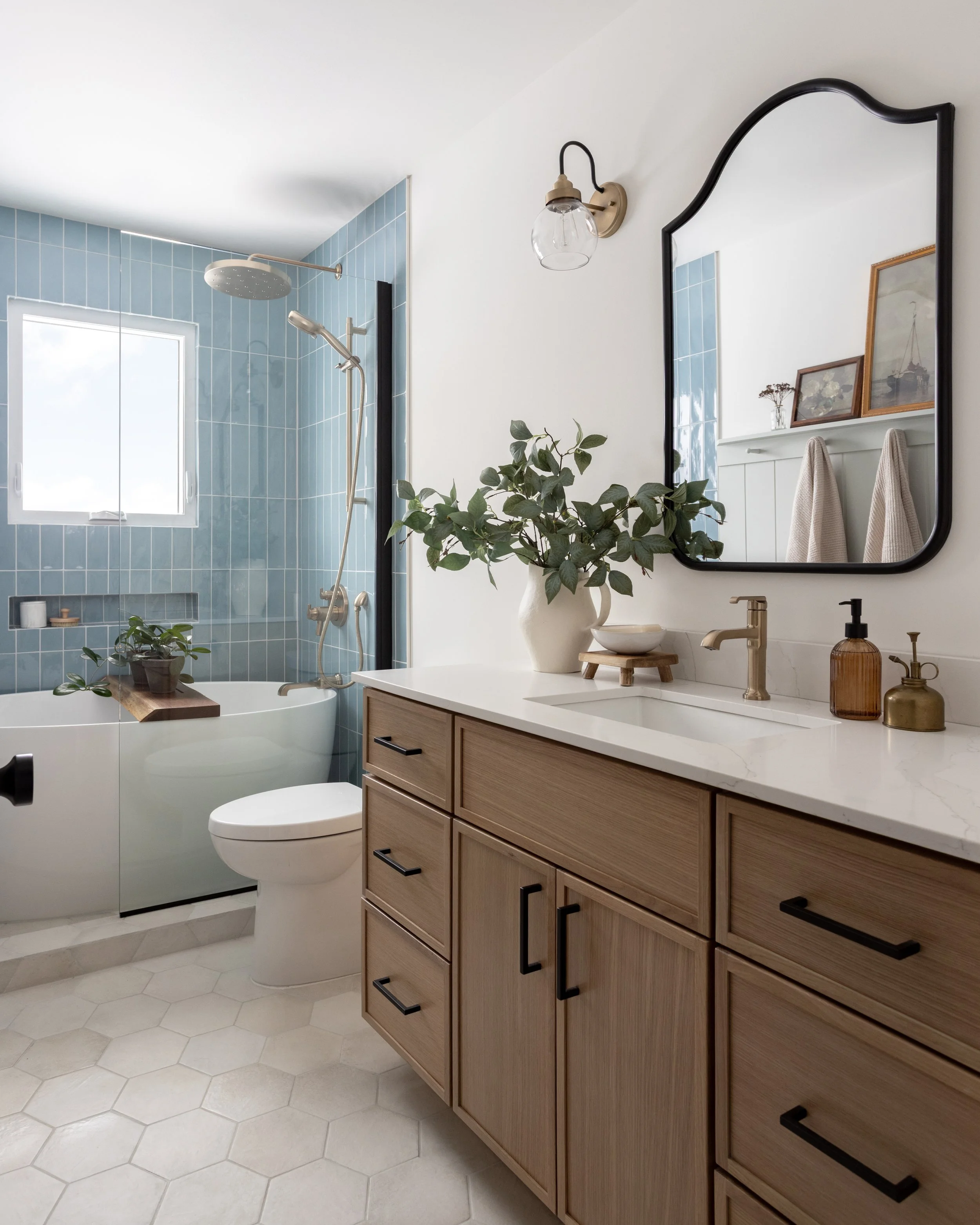 Modern bathroom with a wood vanity, large mirror, potted plant, and a shower with blue tiled walls.