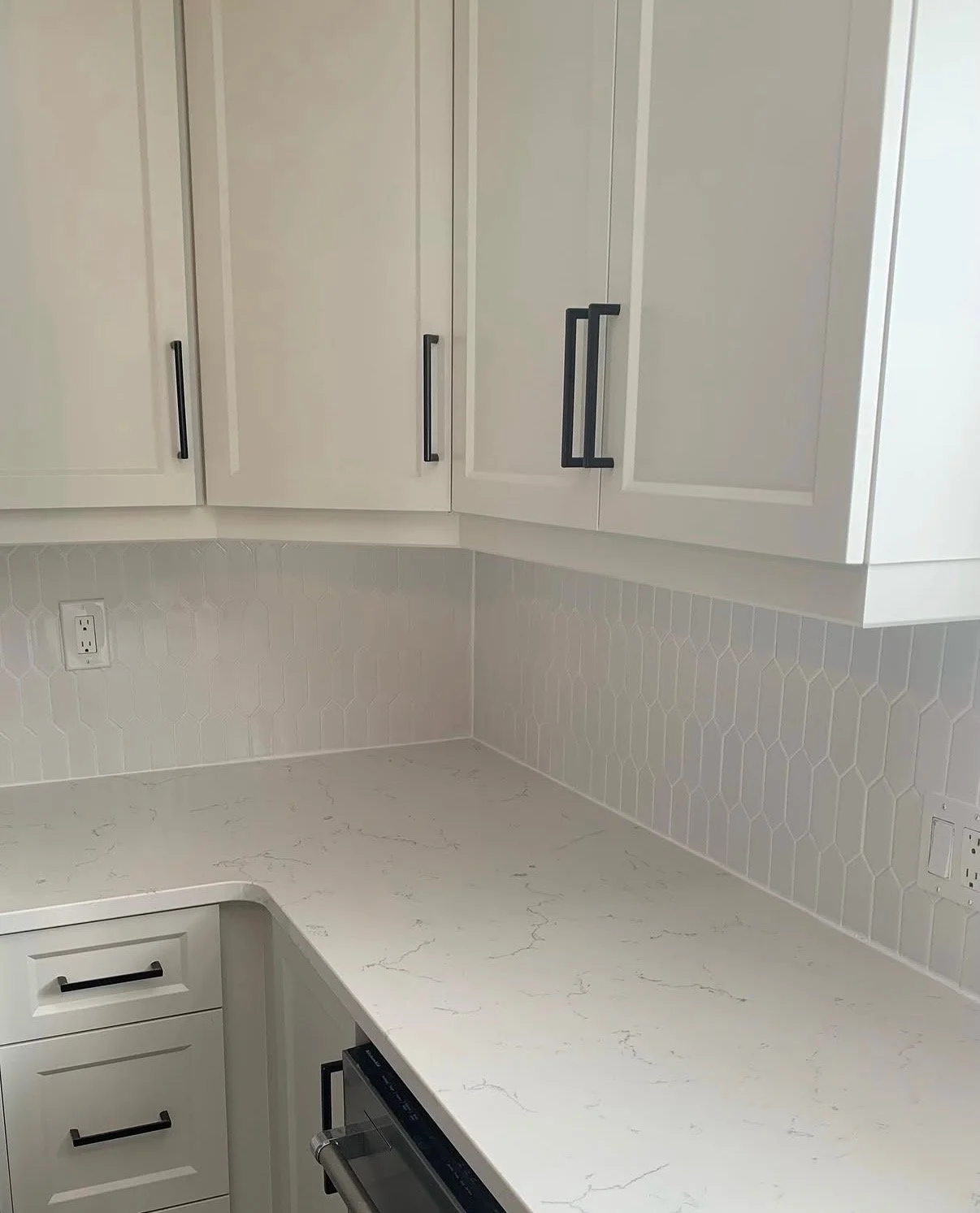Kitchen with white cabinets, black handles, white patterned backsplash, and white marble countertop.