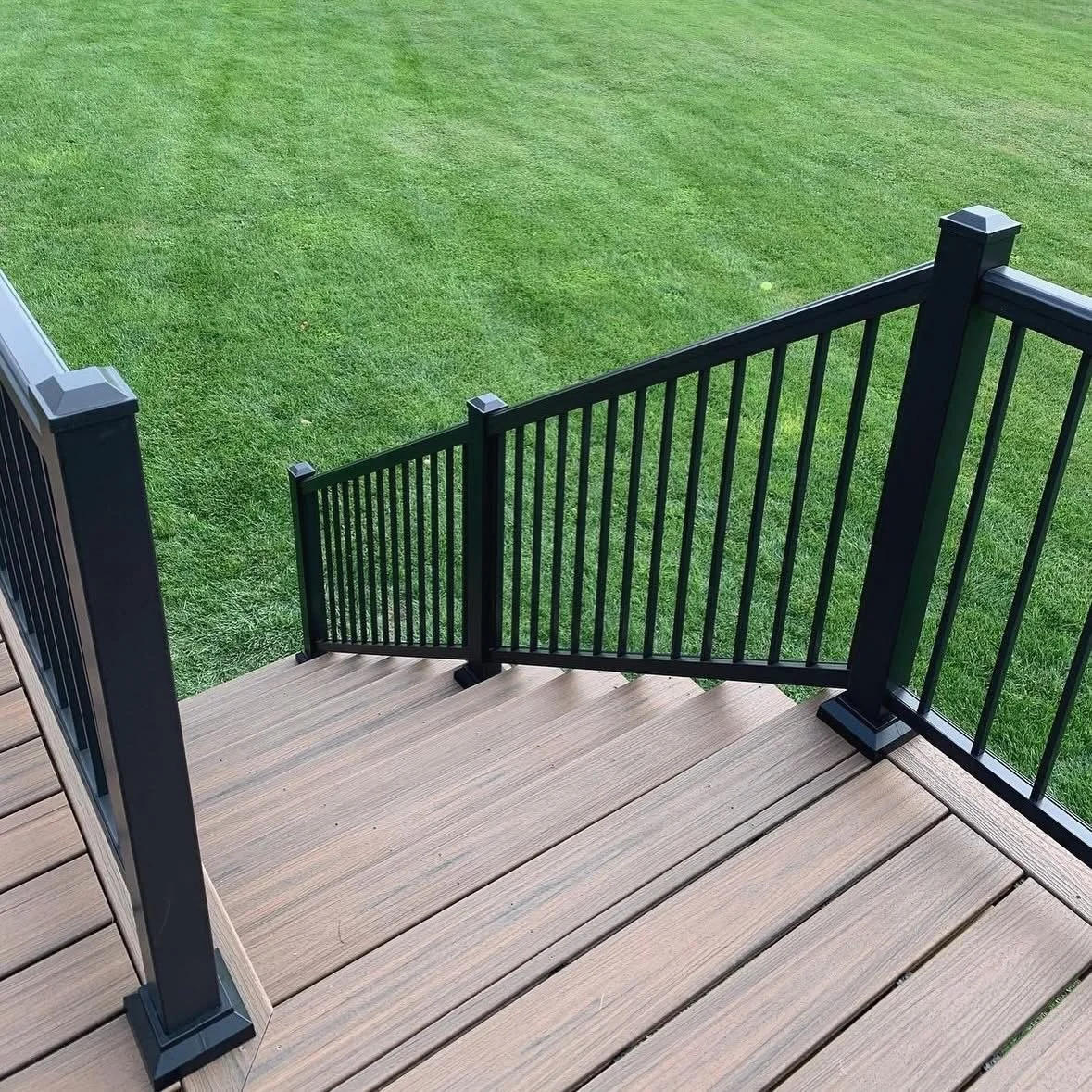 View of a wooden deck with a black metal railing, overlooking a green grassy yard.