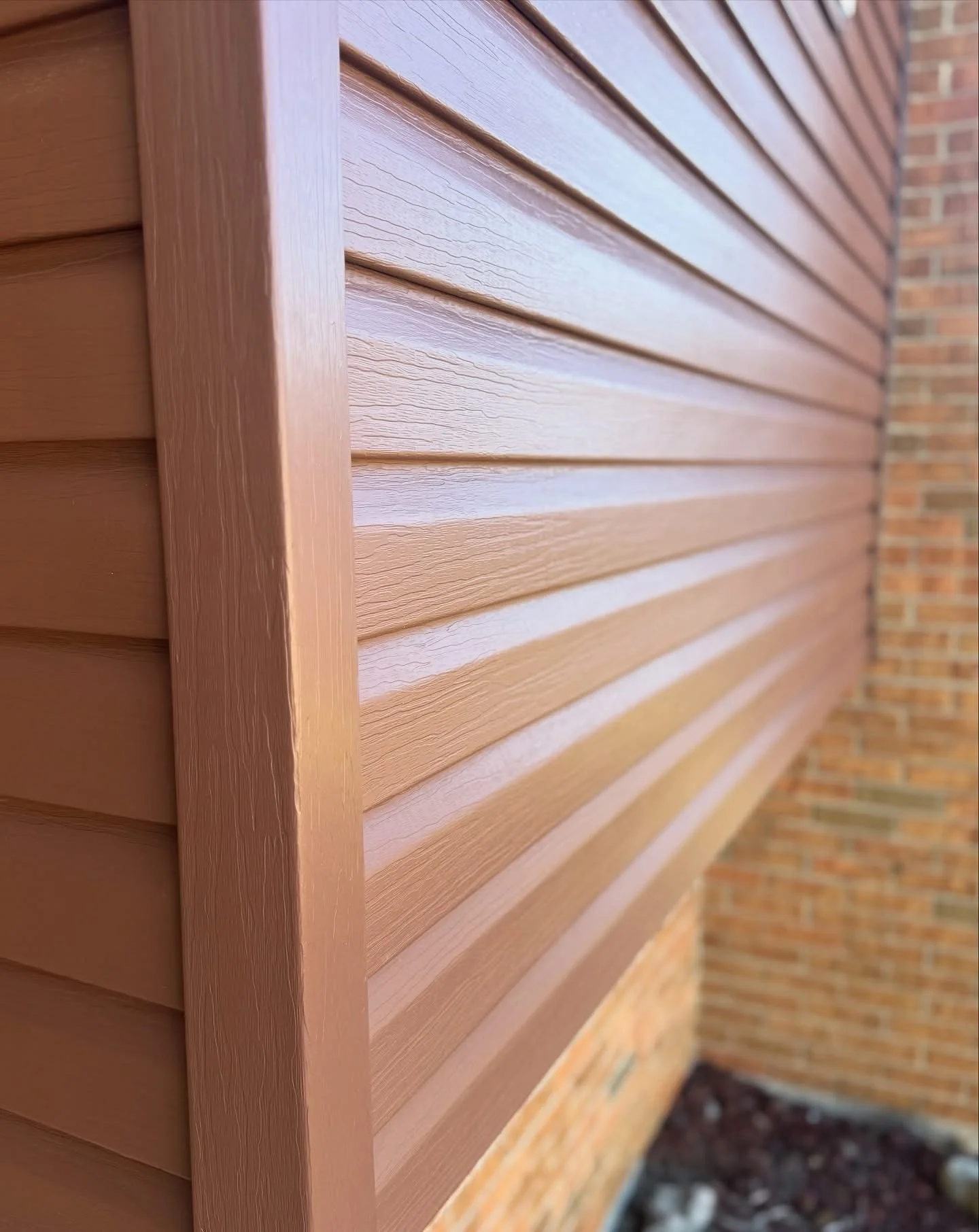Close-up view of horizontal wooden siding on a building with a brick wall in the background.