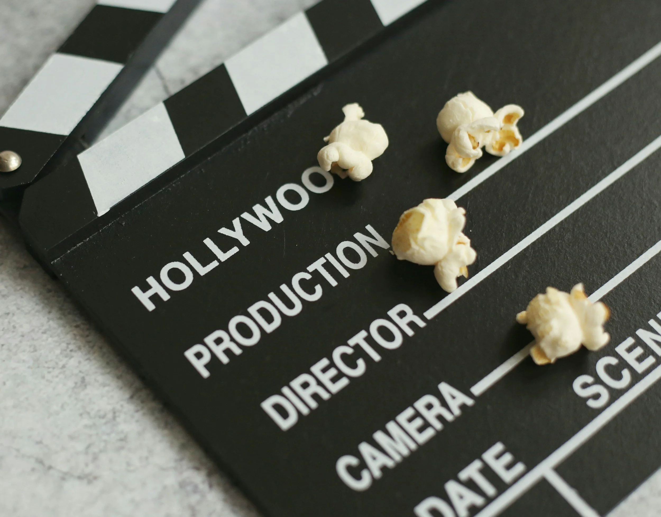 Close-up of a black clapperboard with white text and popcorn pieces on it.