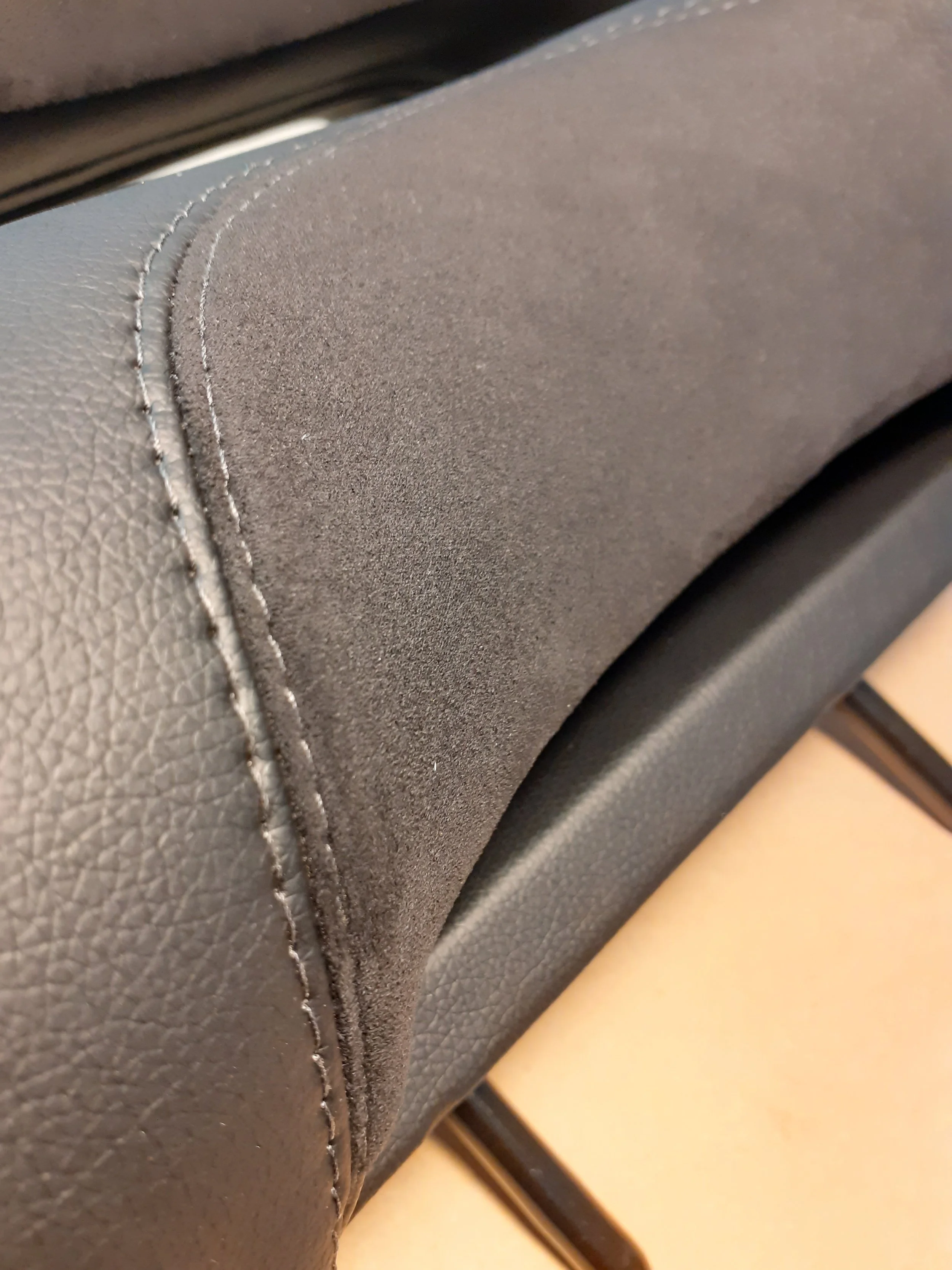 Close-up of a stitched seam on a black leather or faux leather item, possibly furniture or a car seat.