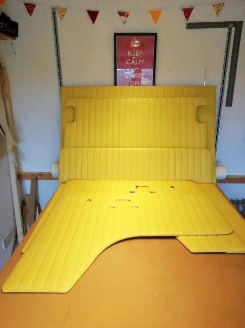 Yellow upholstered headboard and mattress with parts of the mattress removed and laid on a wooden table.