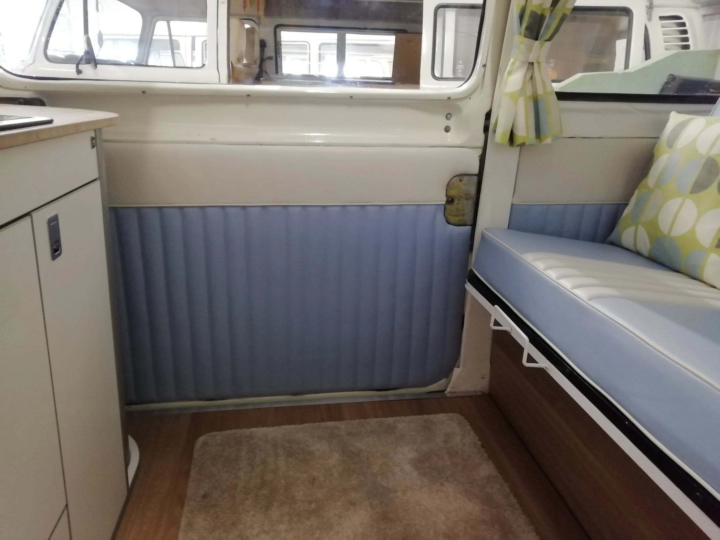 Interior of a vintage camper van with a seating area and a window with a curtain on the right side.