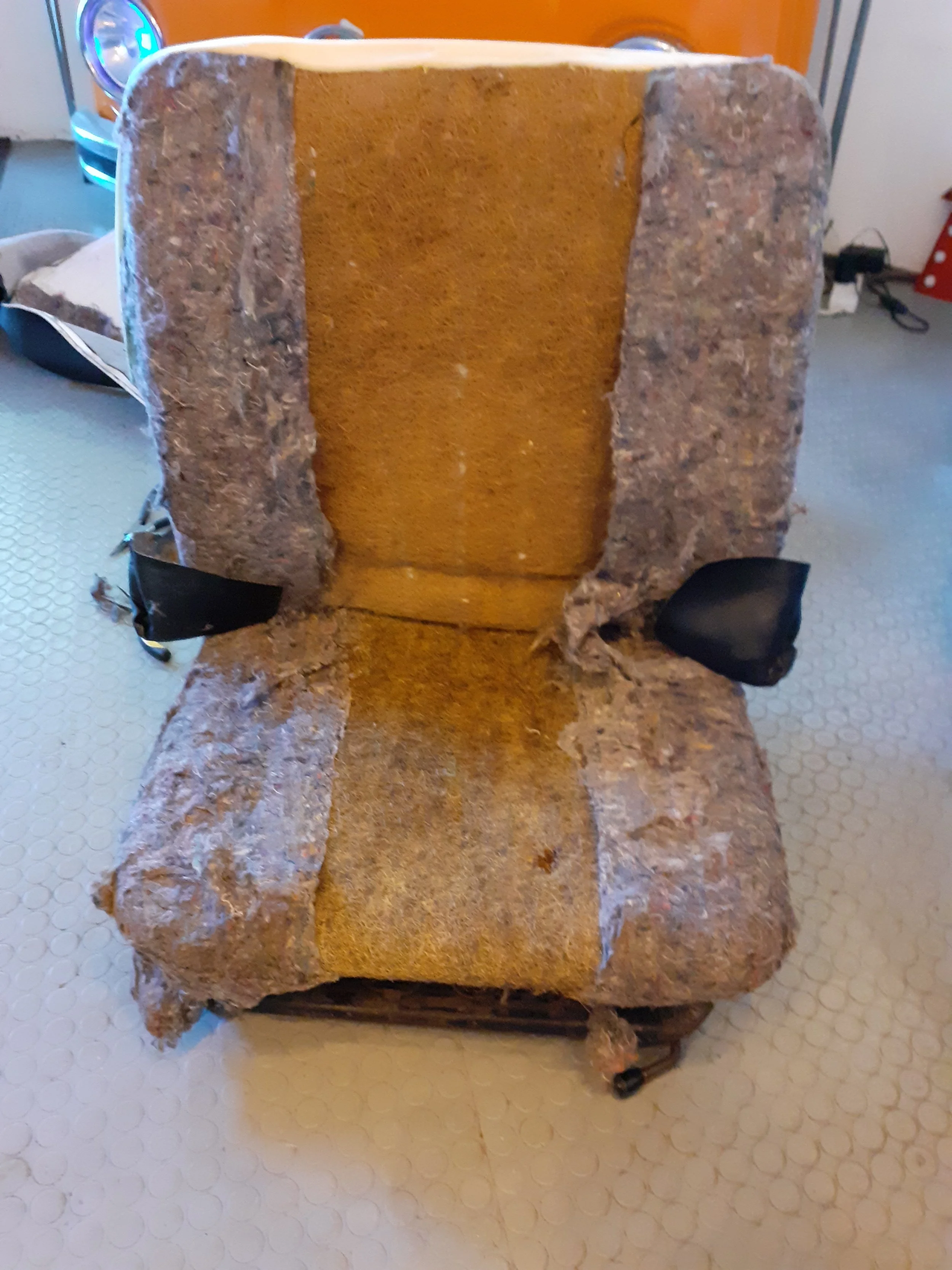 A rock-shaped chair with a soft interior, placed on a light-colored tiled floor, with a black strap attached on one side.