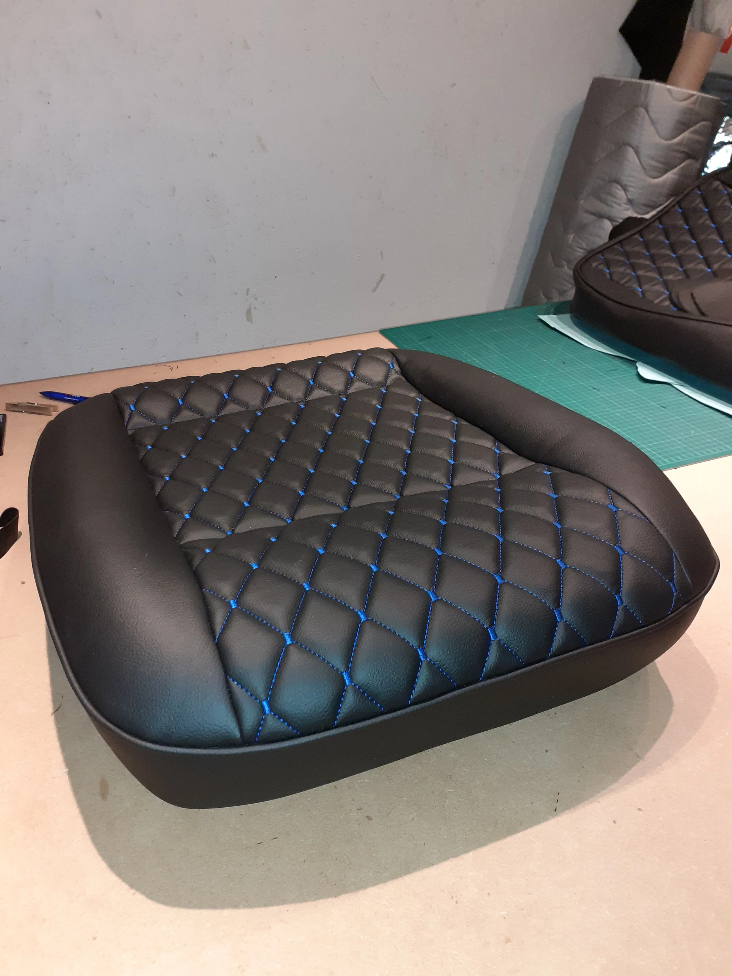 A black cushioned car seat or chair with blue stitching on a work table.