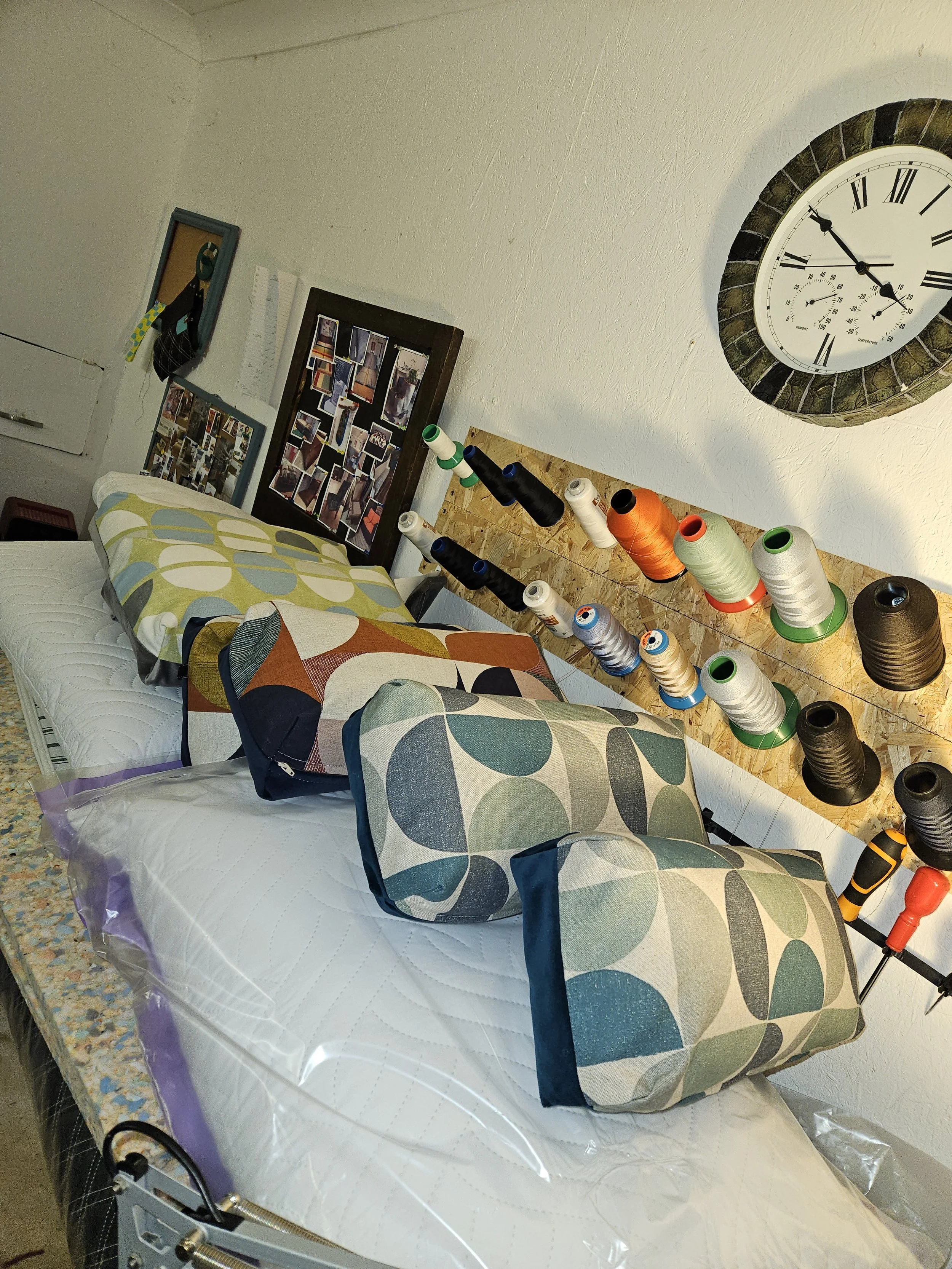 Hospital bed with a patterned pillow, a blanket, and a pillowcase, set up in a room with various decoration items and a large clock on the wall.
