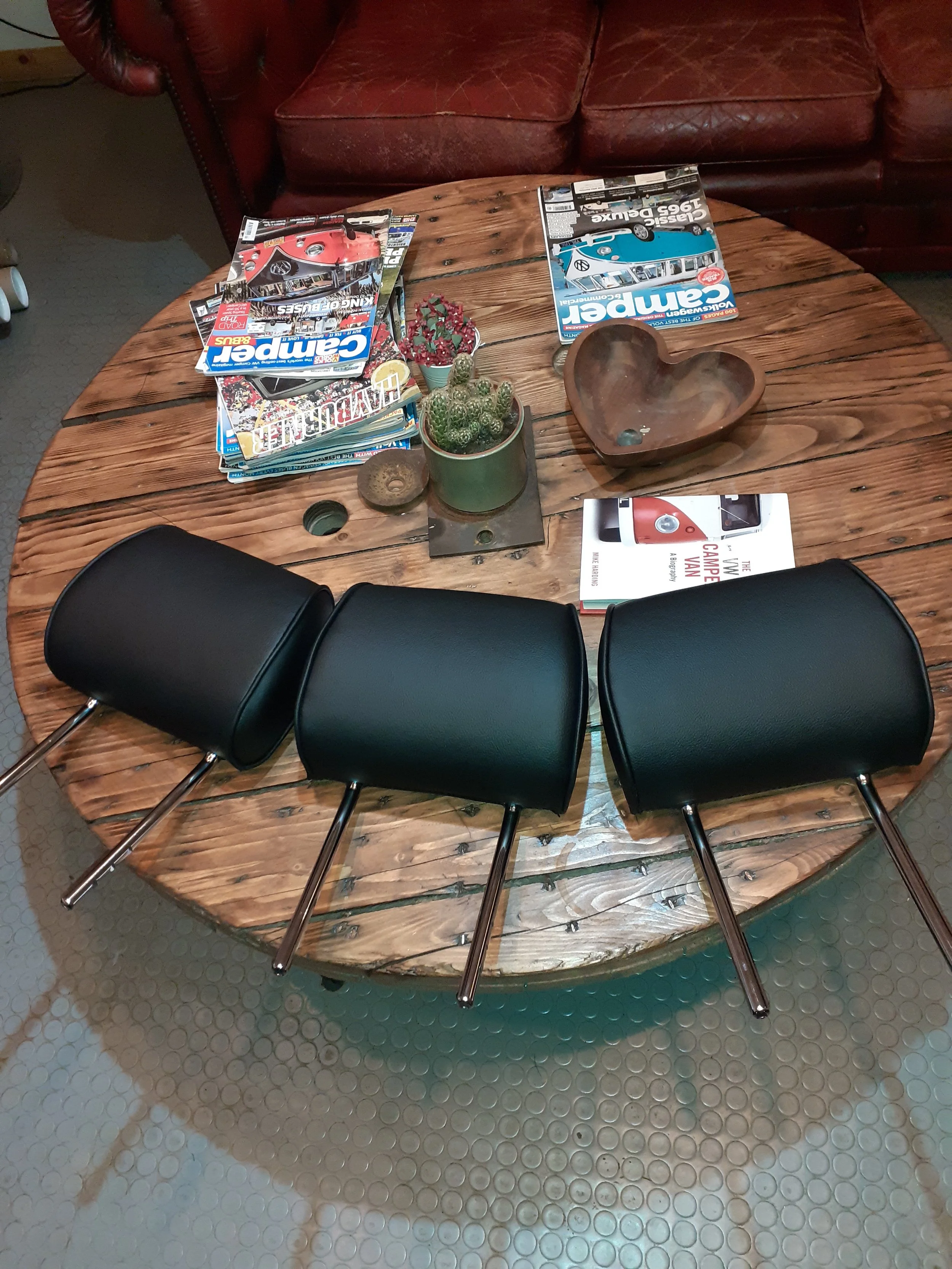 Round wooden table with black chairs, magazines, potted plants, and a decorative wooden bowl on top of the table.