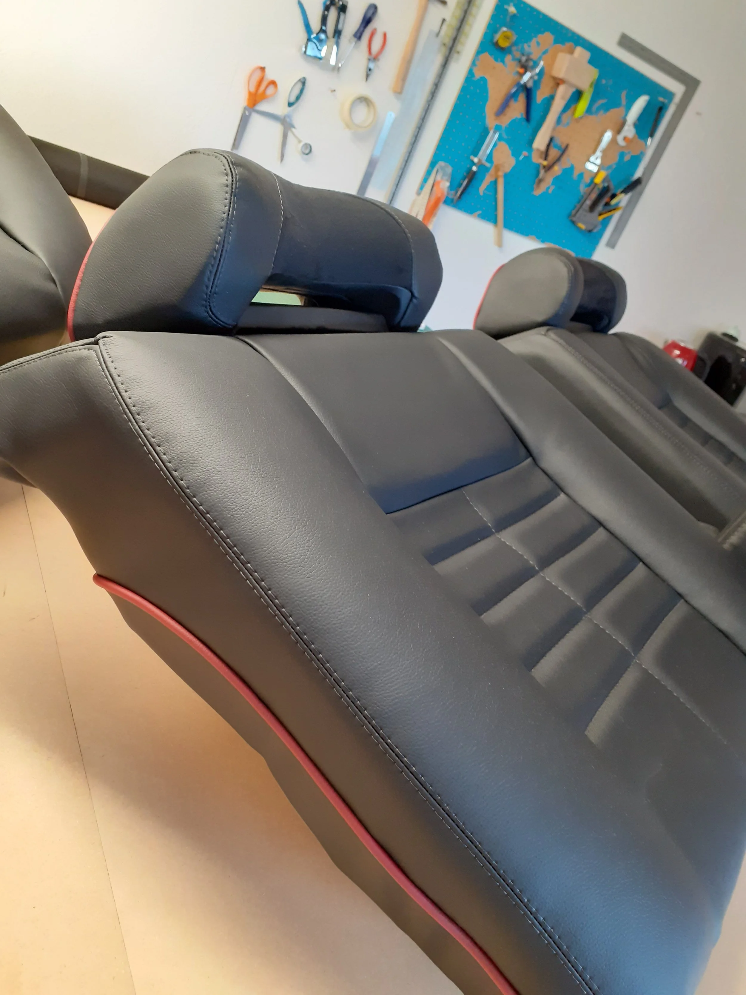 A black leather sofa with pink trim in a room, with a workbench and tools on the wall in the background.