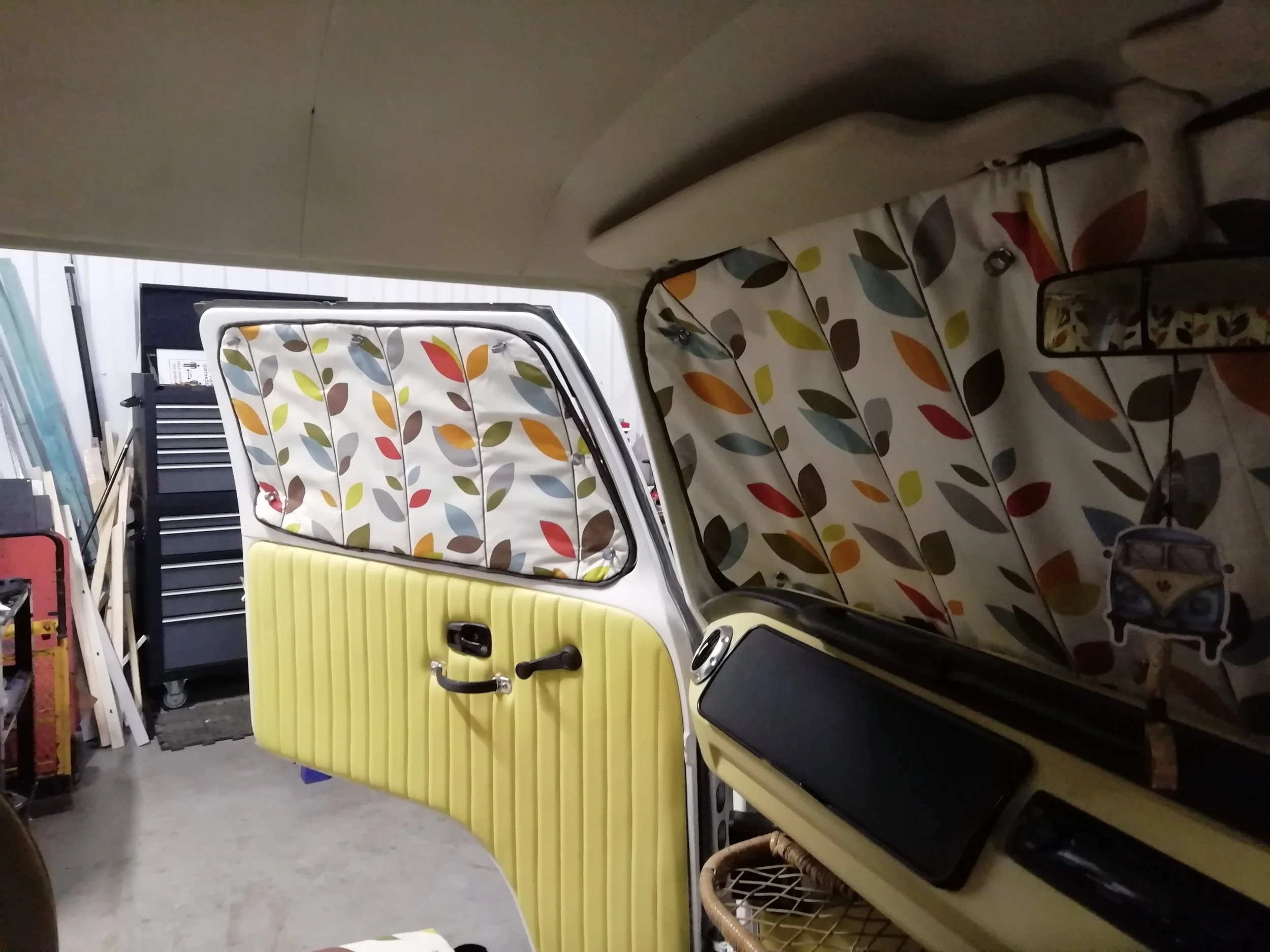 A storage room with various household items, including a yellow upholstered chair, a metal frame with a floral patterned fabric, a black tool chest, and miscellaneous household supplies.