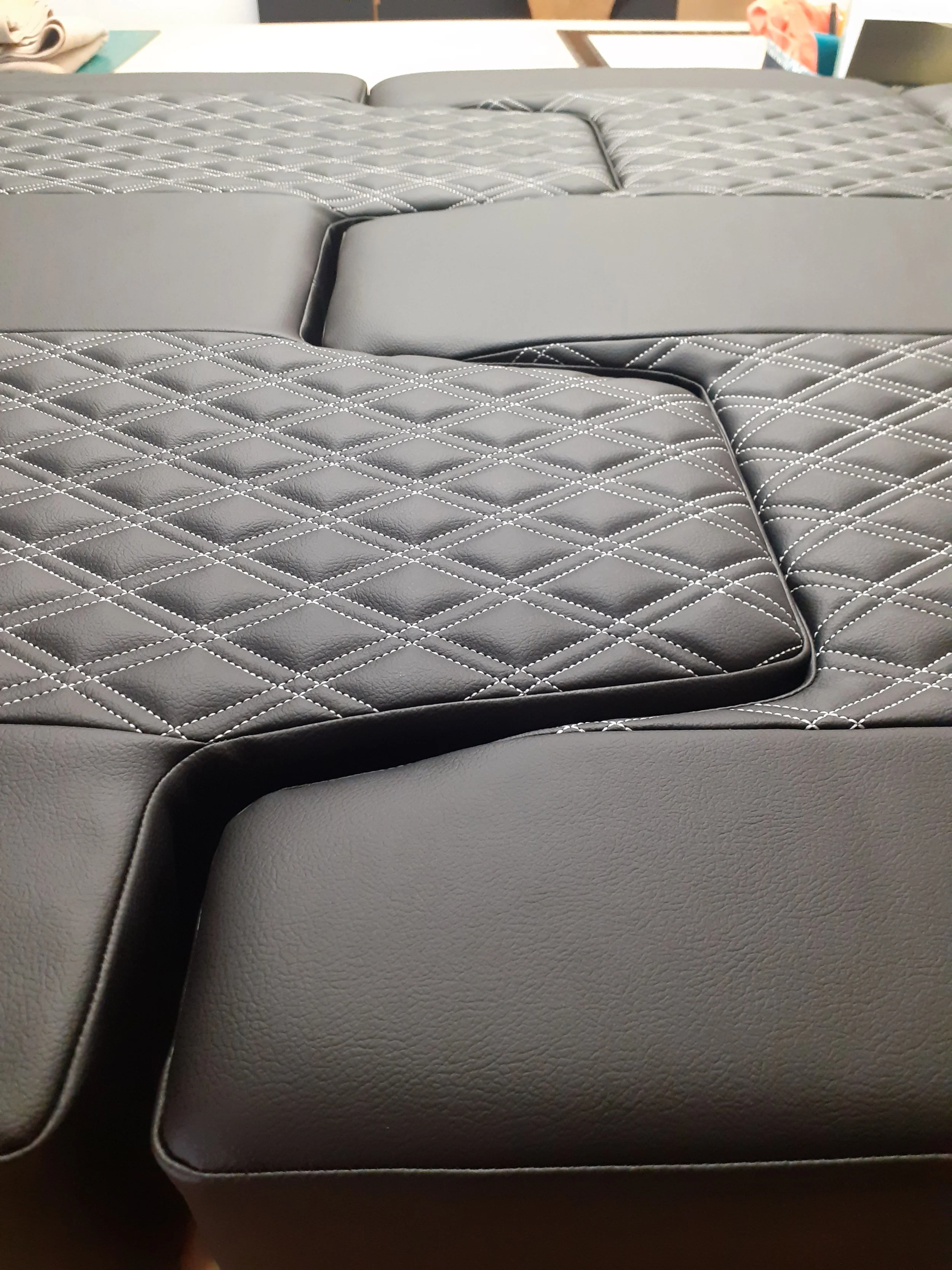 Close-up of black quilted leather car seat with white stitching.