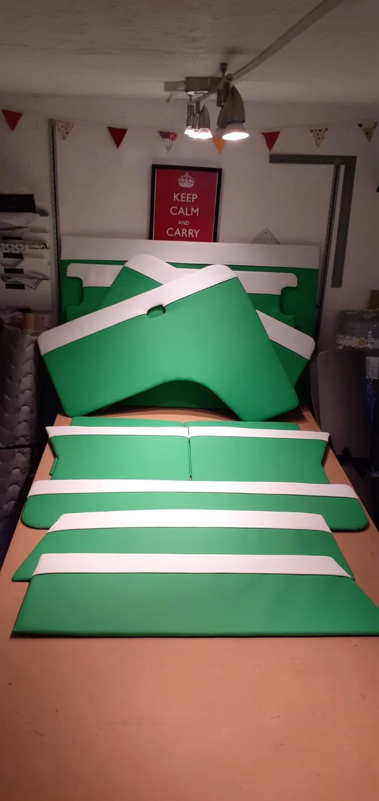Disassembled green and white meeting or classroom chairs arranged on a table, with a framed poster in the background that says 'Keep Calm and Carry On', and bunting hanging from the ceiling.