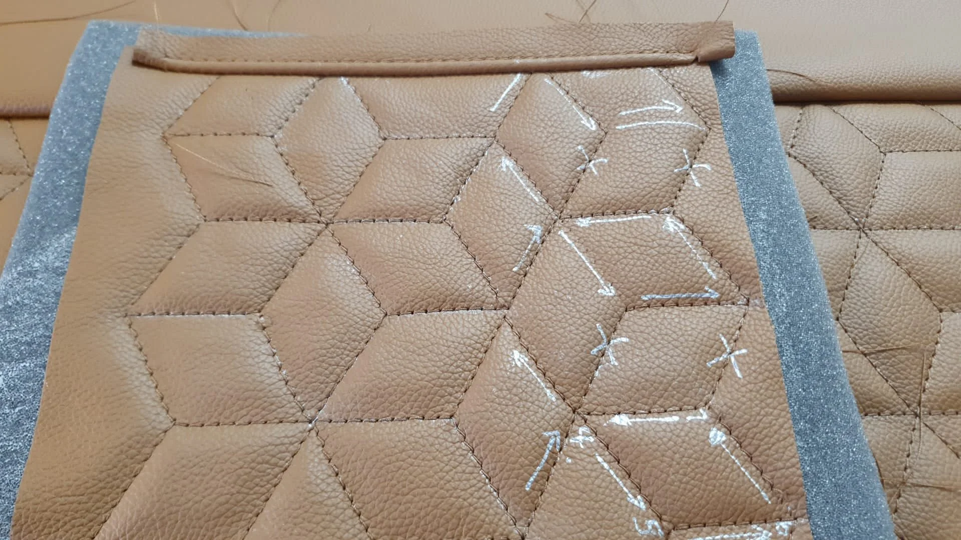 A piece of tan leather with diamond-shaped stitching and white markings, with strips of silver glitter tape on the sides.