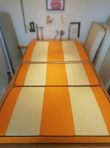 Three tables with orange and yellow striped tabletop covers placed next to each other in a room with wall decorations and chairs.