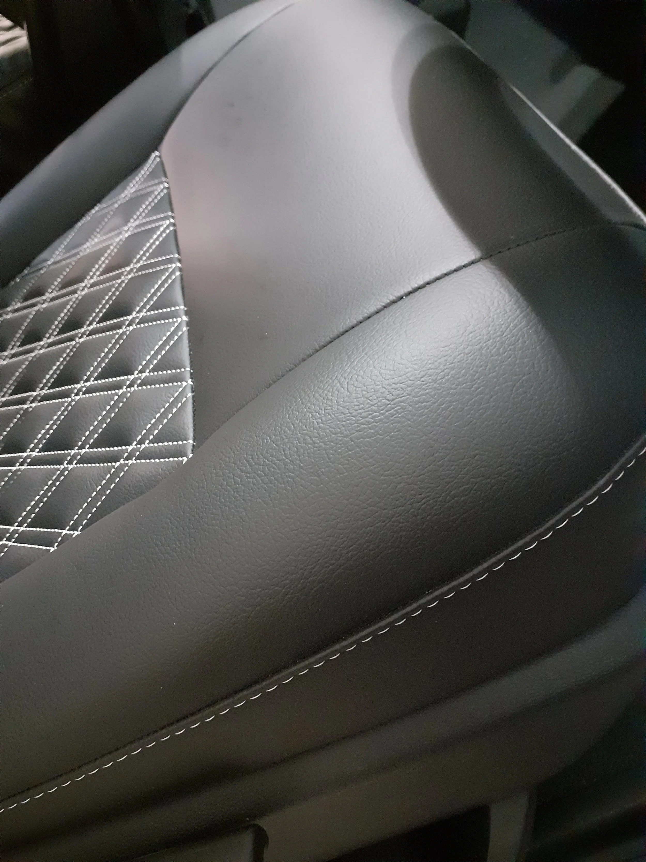 Close-up image of car seat upholstery showing a combination of plain and diamond-quilted black leather with white stitching.