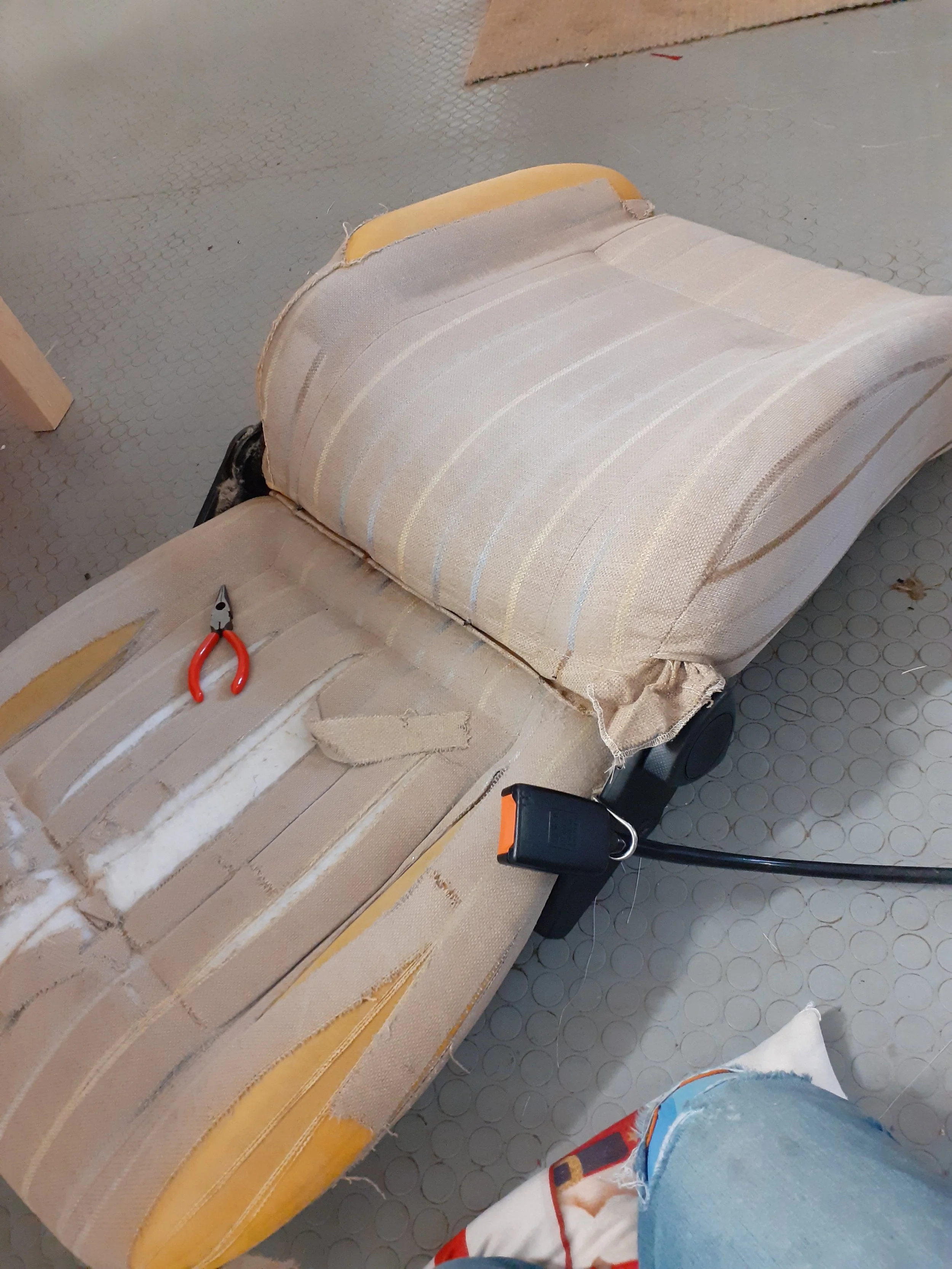Close-up of a piece of furniture under construction, with fabric and tools on a textured gray floor.