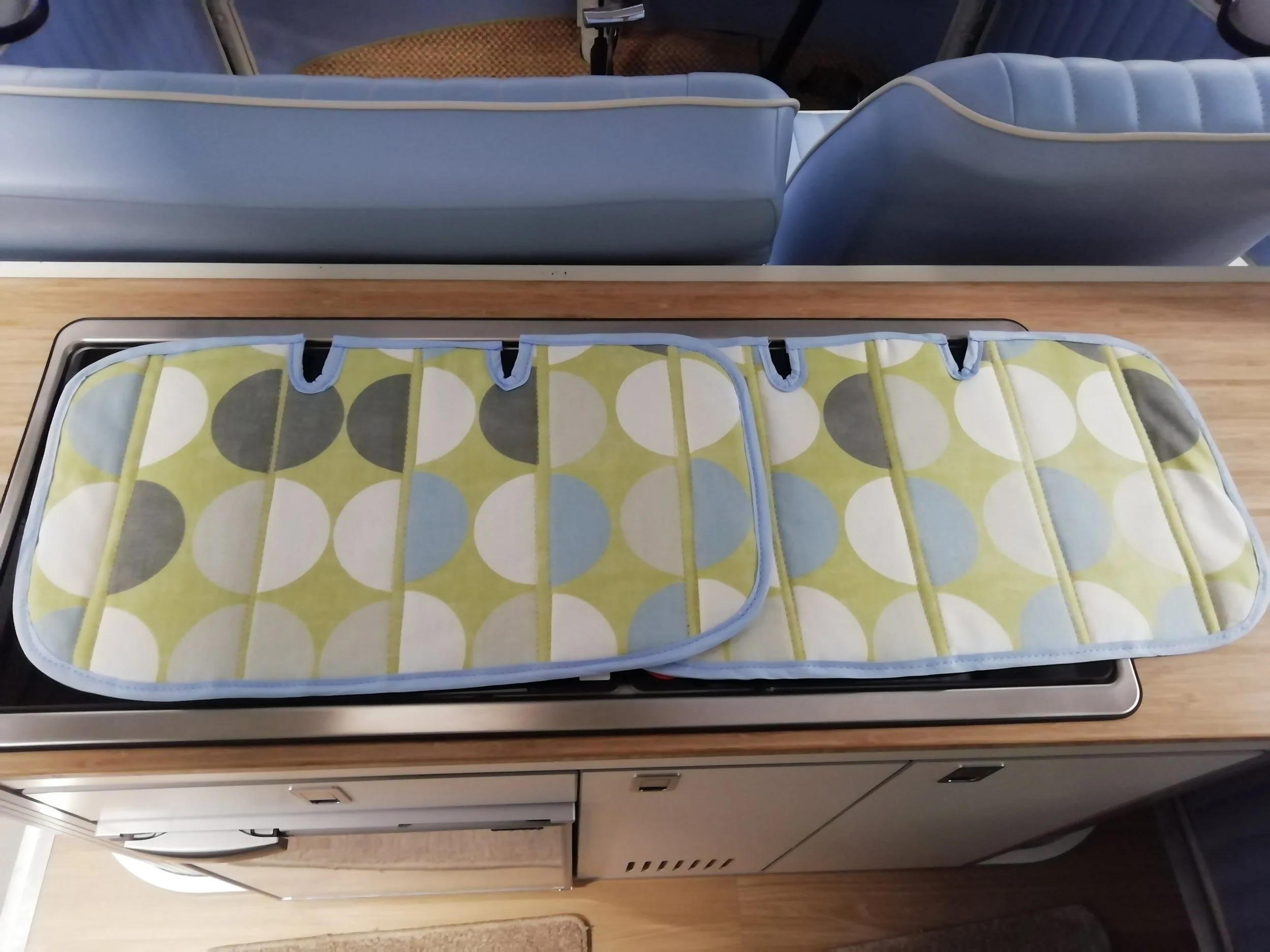 Close-up of a retro-style tray with a yellow, white, green, and gray dotted pattern, placed on top of a counter or table in front of a row of vintage blue and gray airline seats.